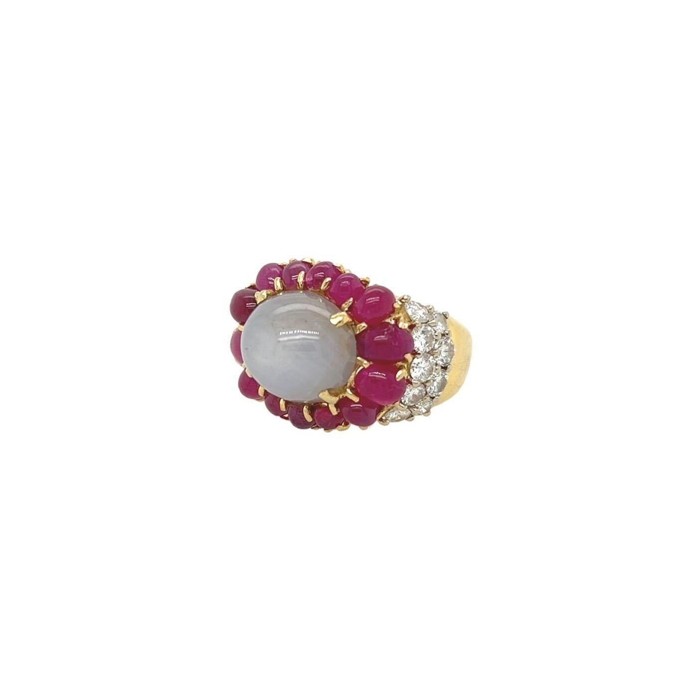 An 18 karat yellow gold, star sapphire, ruby and diamond ring.  Centering an oval gray star sapphire measuring approximately 13.83 x 11.01 mm surrounded by fourteen (14) oval cabochon rubies and set at each shoulder with nine (9) round brilliant cut