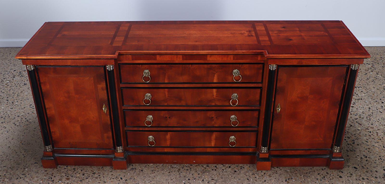 A Yew wood Empire style sideboard or credenza by Century. The case has ebonized columns flanking the doors and lion head brass drawer pulls.