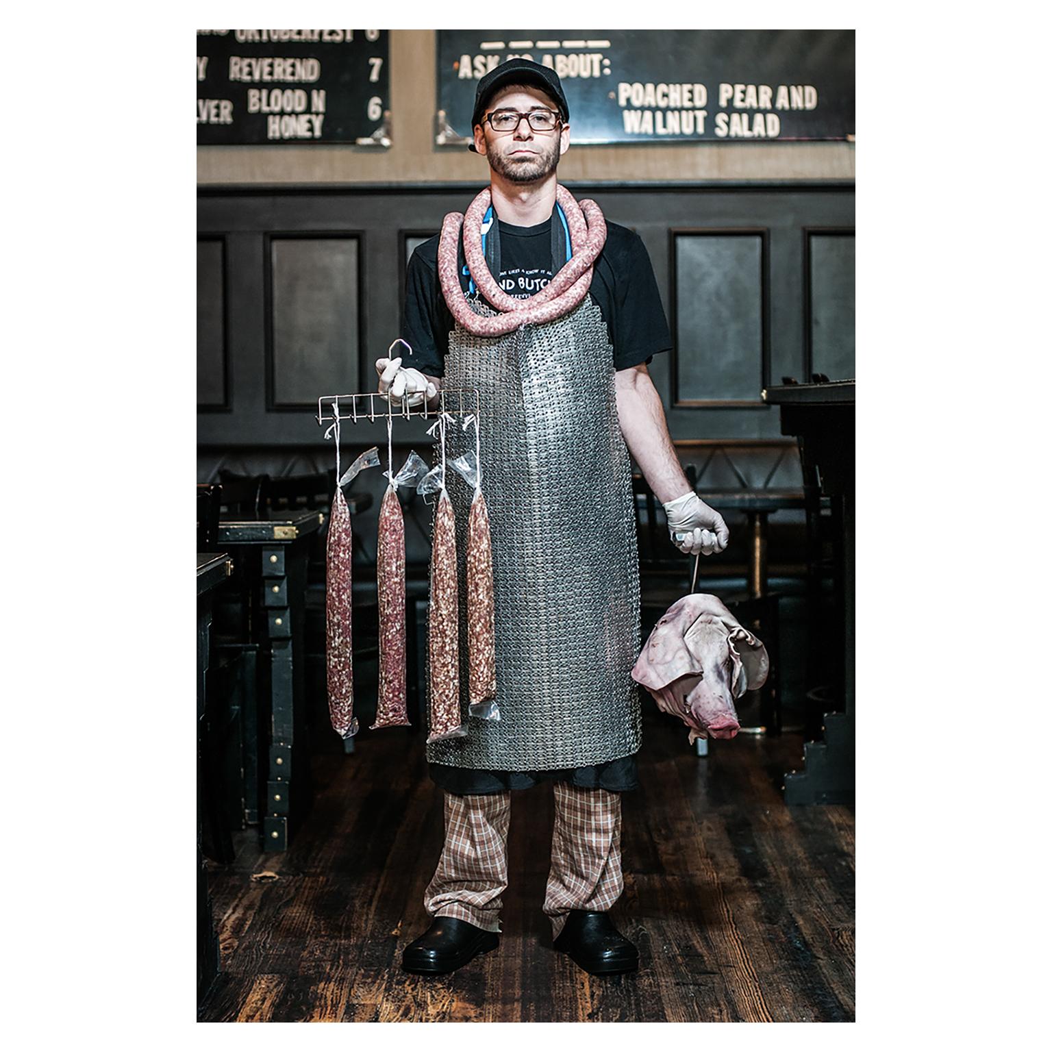 Butcher by Can Turkyilmaz. Photograph of butcher with sausages and pigs head For Sale 2
