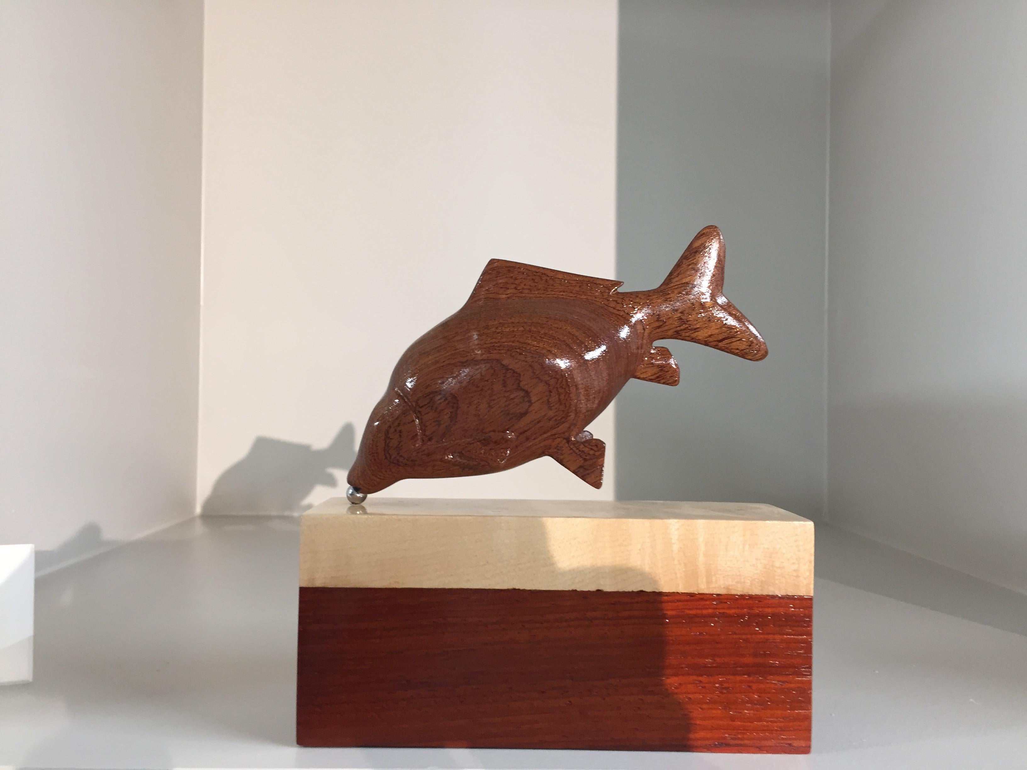 This Sculpture is made by Jos de Wit. It is made of mahogany wood. The pedestal is made of mahogany and maple wood. In the not of the fish there is a piece of mother-of-pearl, just like he uses for building his string instruments. The wood, and al