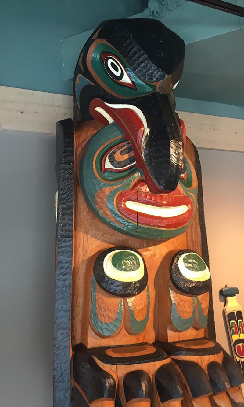 Carved in the round, this red cedar totem pole depicts Raven, a clan crest from Tlingit/Kwaguitl of Tom’s fathers’ chiefs house. They possess seven coppers with the chiefs’ position; the copper is the shield shape held horizontally in the bottom