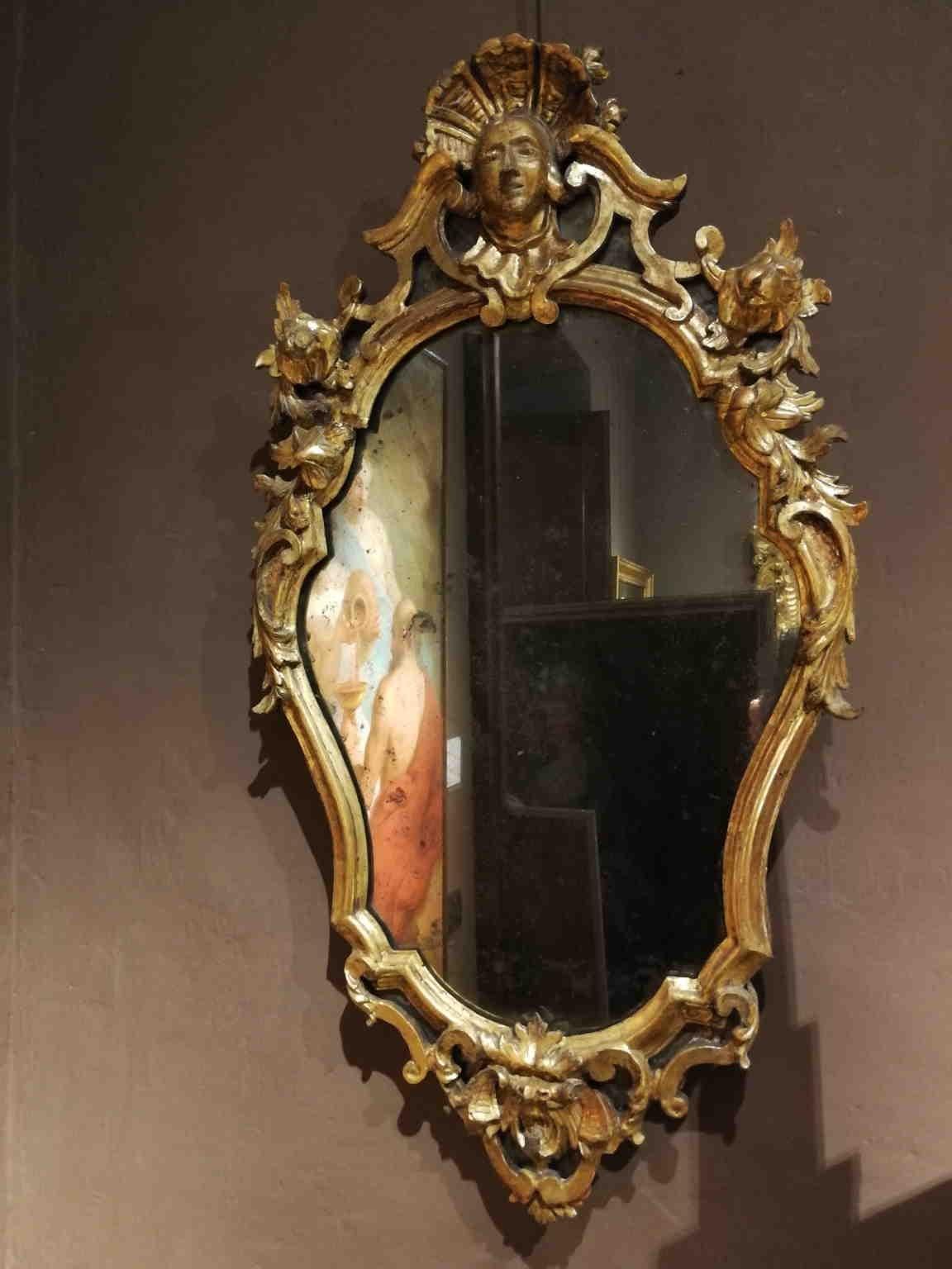 Those pair of Rococo wall mirrors maintained their original glasses.
They are made of gilded wood carved with a grotesque decoration characterized by coil of flowers. At the top there is a female head with a feather crown, while at the bottom a