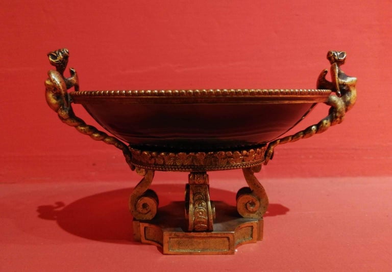 The object consists in a cup in carnelian inserted on a gilded and chiselled bronze support. The handles have the shape of an harpy, the edge is adorned with a perlée ferrule and the circular base has a espalier decoration. The pedestal is composed