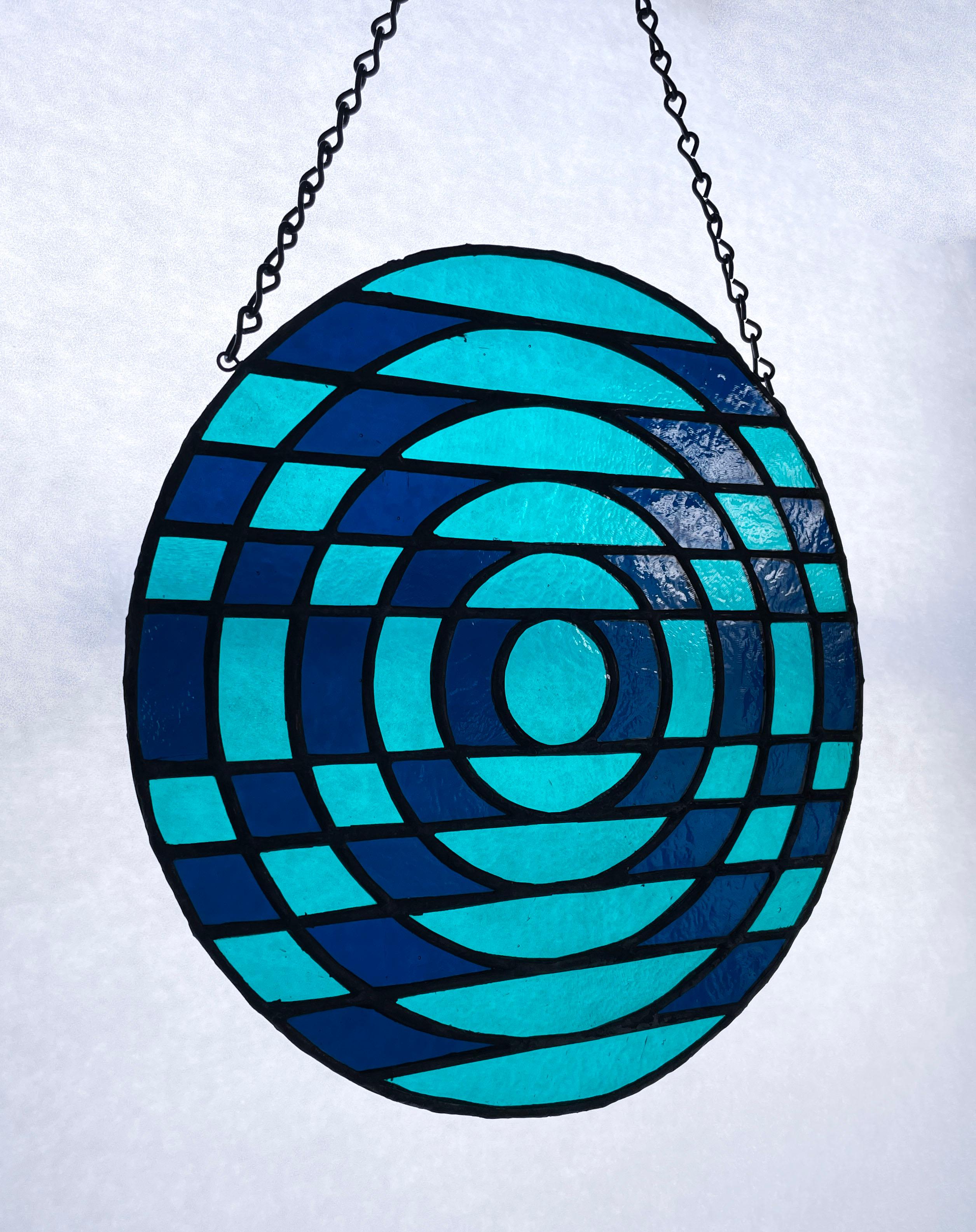 Handcrafted by TF Dutchman, Japanese Optical is a one of a kind original stained glass window panel. This piece uses Bullseye transparent copper blue and teal cathedral glass and hangs on a chain. Please feel free to inquire about custom colors and