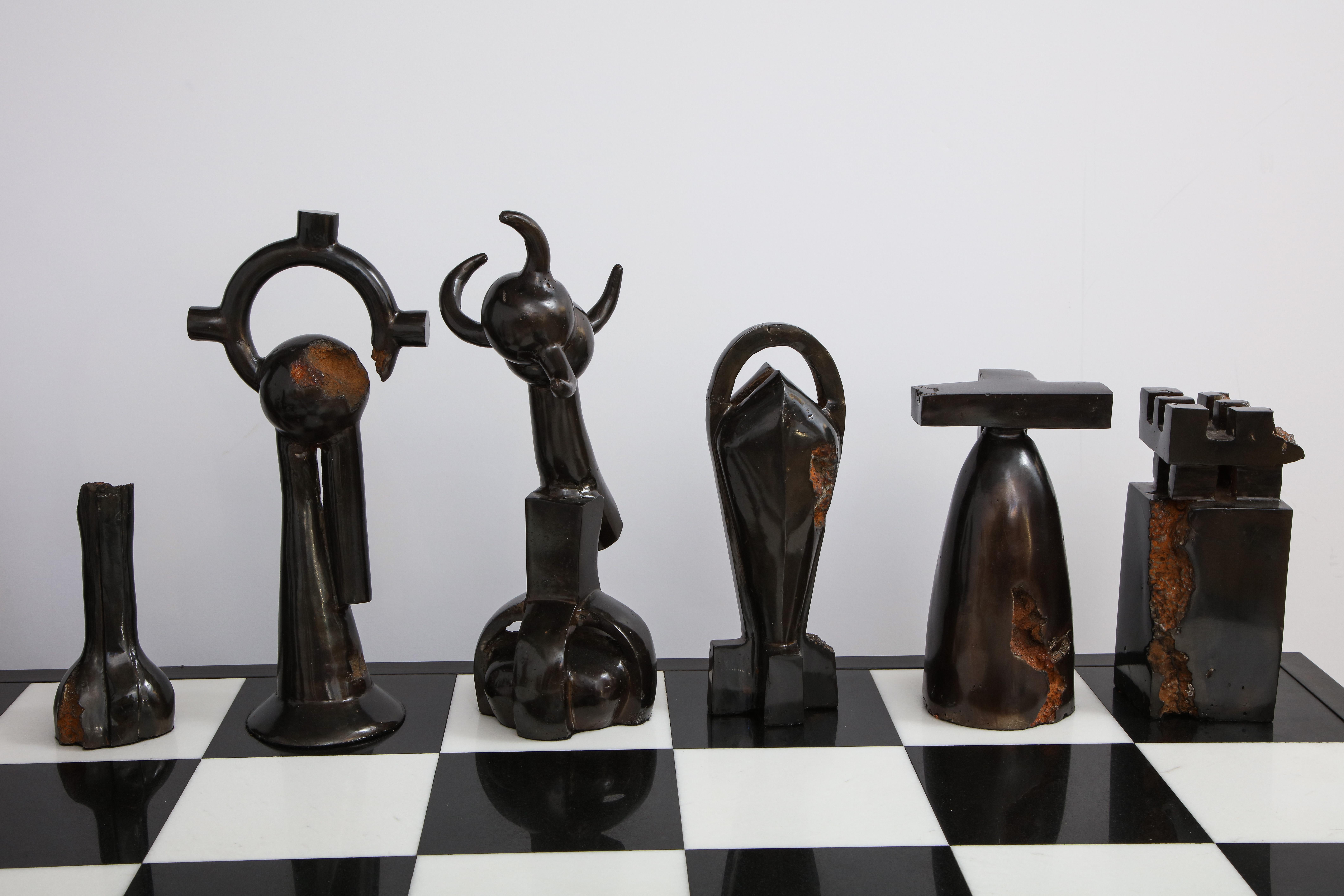 Comprising: 16 Bronze & 16 Iron Chess pieces of different heights, Edition 2/2, along with a chess board having a wood boarder around a black onyx and carerra white marble center.
