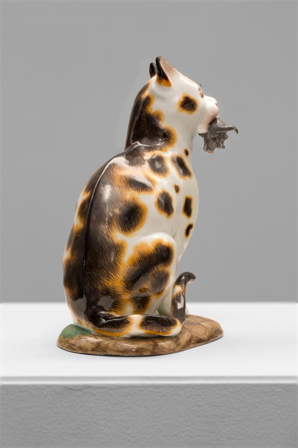 This charming figurine from Meissen Porcelain is of a cat with a captured mouse in his mouth, seated on its haunches, its left forepaw raised to strike the mouse dangling from its mouth, with white coat, brown stripes and spots, and on a ground