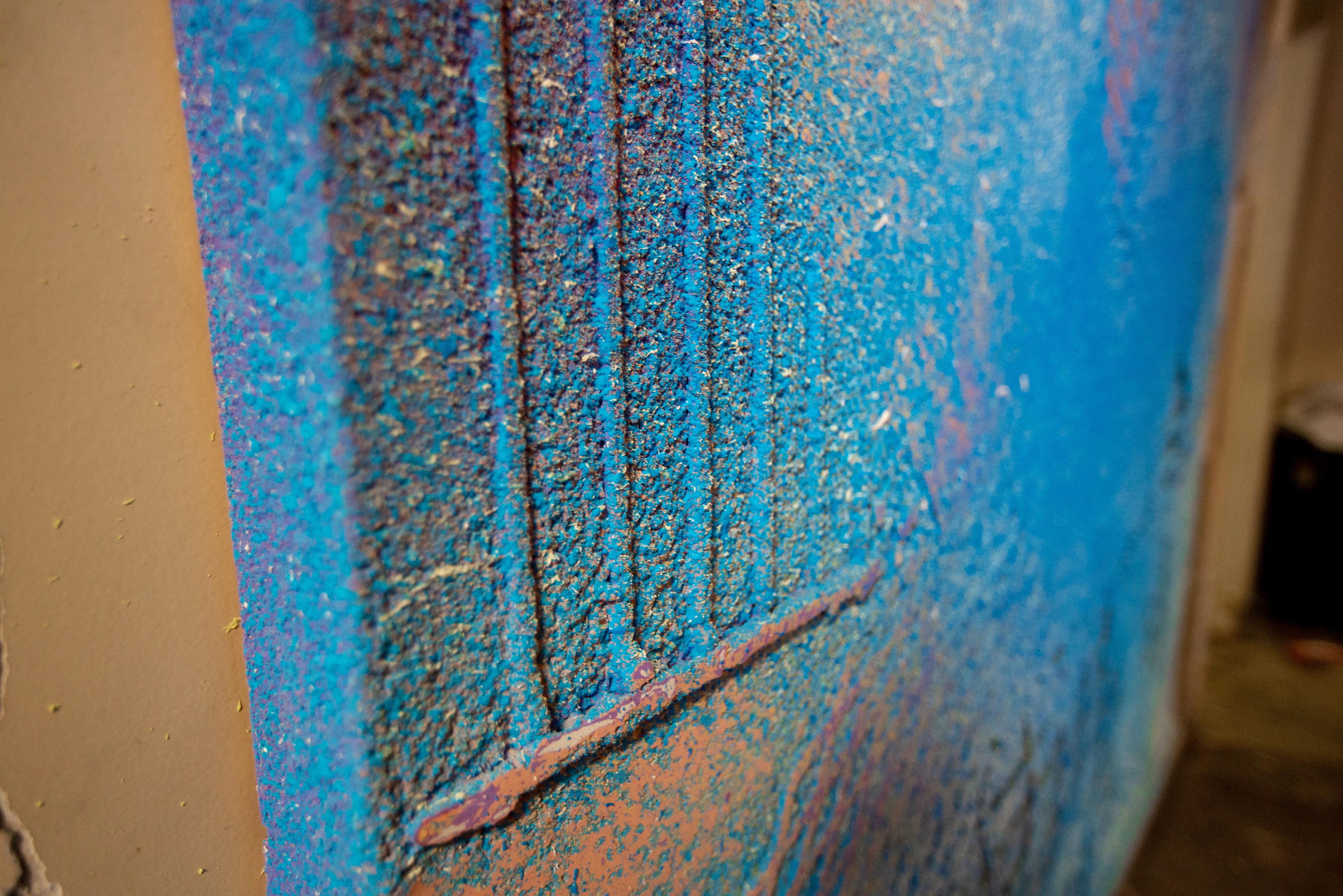 This unique piece is a splash of mixed colors, figures and shapes to create a plethora of textures. The piece is predominantly in shades of blue, though it has a mixture of yellows, splashes of purple and orange in different parts of the piece. This