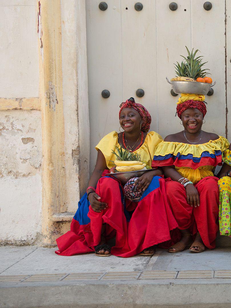 Four Palenqueras - Cartagena, Colombia fruit sellers in red, yellow & blue - Photograph by Lou Vest