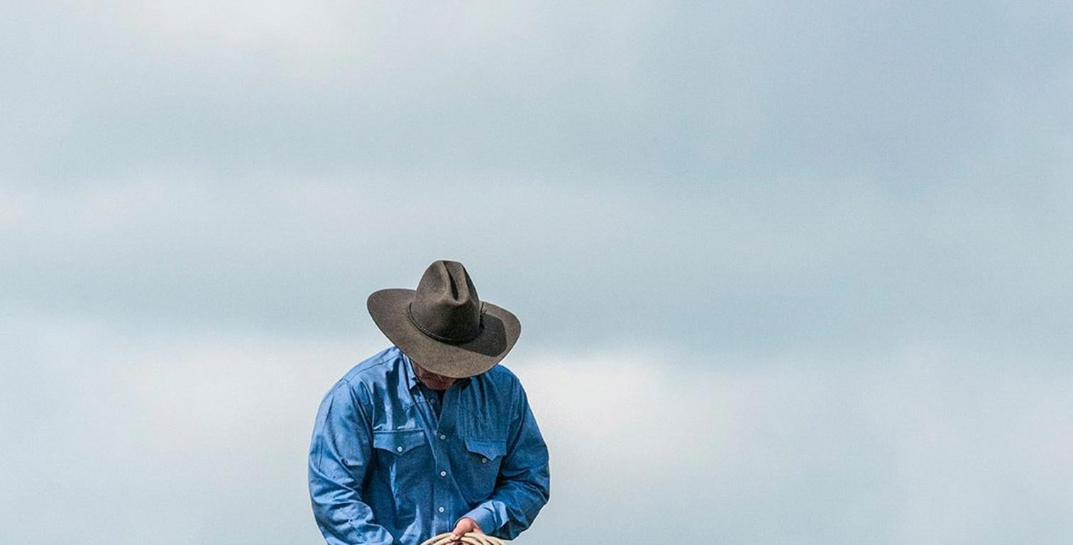 Weary Cowboy - Texas man in blue shirt & gray hat riding brown & white horse - Photograph by Alan Montgomery