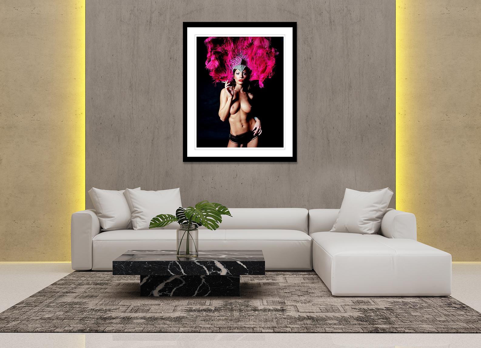 This 2006 fine art print features a nude shot of a beautiful dancer smoking, on a black background that gives a magnificent contrast to her bright pink headdress. The photograph is from John Stoddart’s, “Risqué” series, where he explored a form of