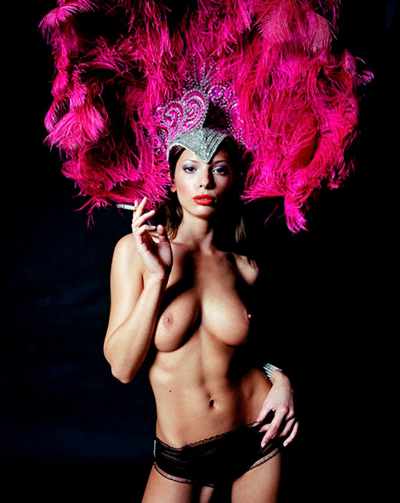 Cette impression d'art de 2006 présente une photo de nu d'une belle danseuse en train de fumer, sur un fond noir qui offre un magnifique contraste avec sa coiffe rose vif. Cette photographie est tirée de la série "Risqué" de John Stoddart, qui a