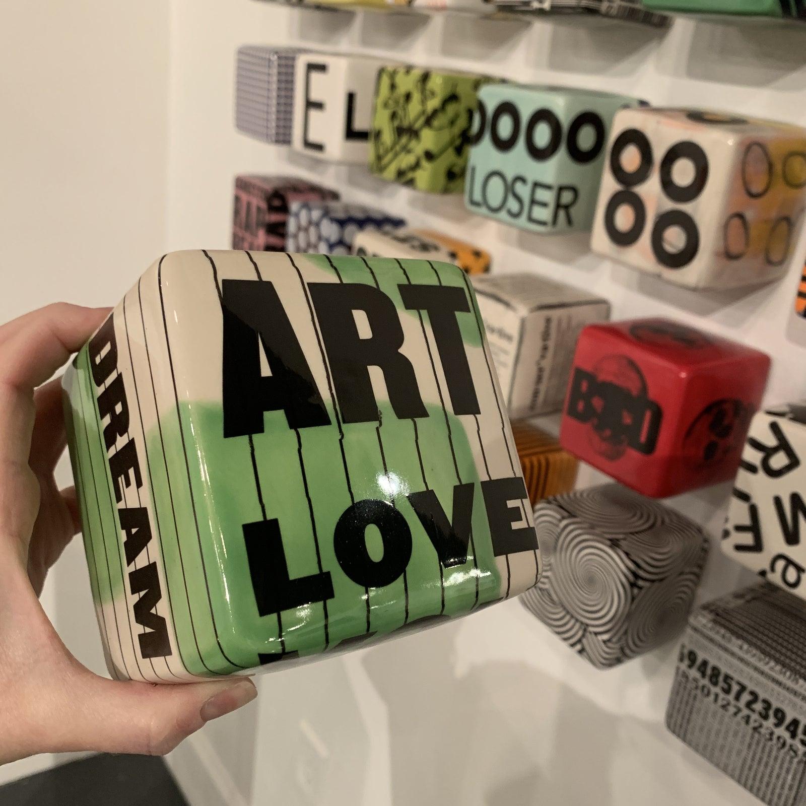 Artist: Kaiser Suidan
4 x 4 x 4 Ceramic Cube with Decal
Can be easily hung or displayed

Quote on the Cube reads: ART LOVE PLAY in green, black and white 