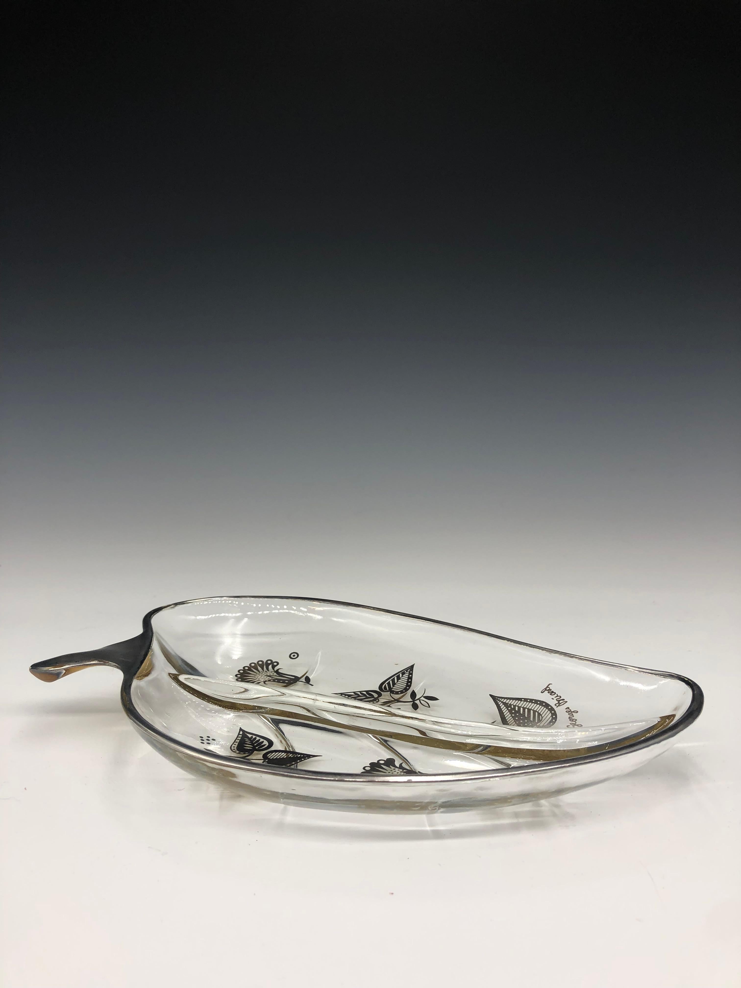 Vintage 1960s Georges Briard clear leaf shape tray/dish with silver floral detail. The piece has a divider that goes down the center. Signed lower right. It can be used as a candy, nut, relish dish, or a catch-all. 

Georges Briard was an American