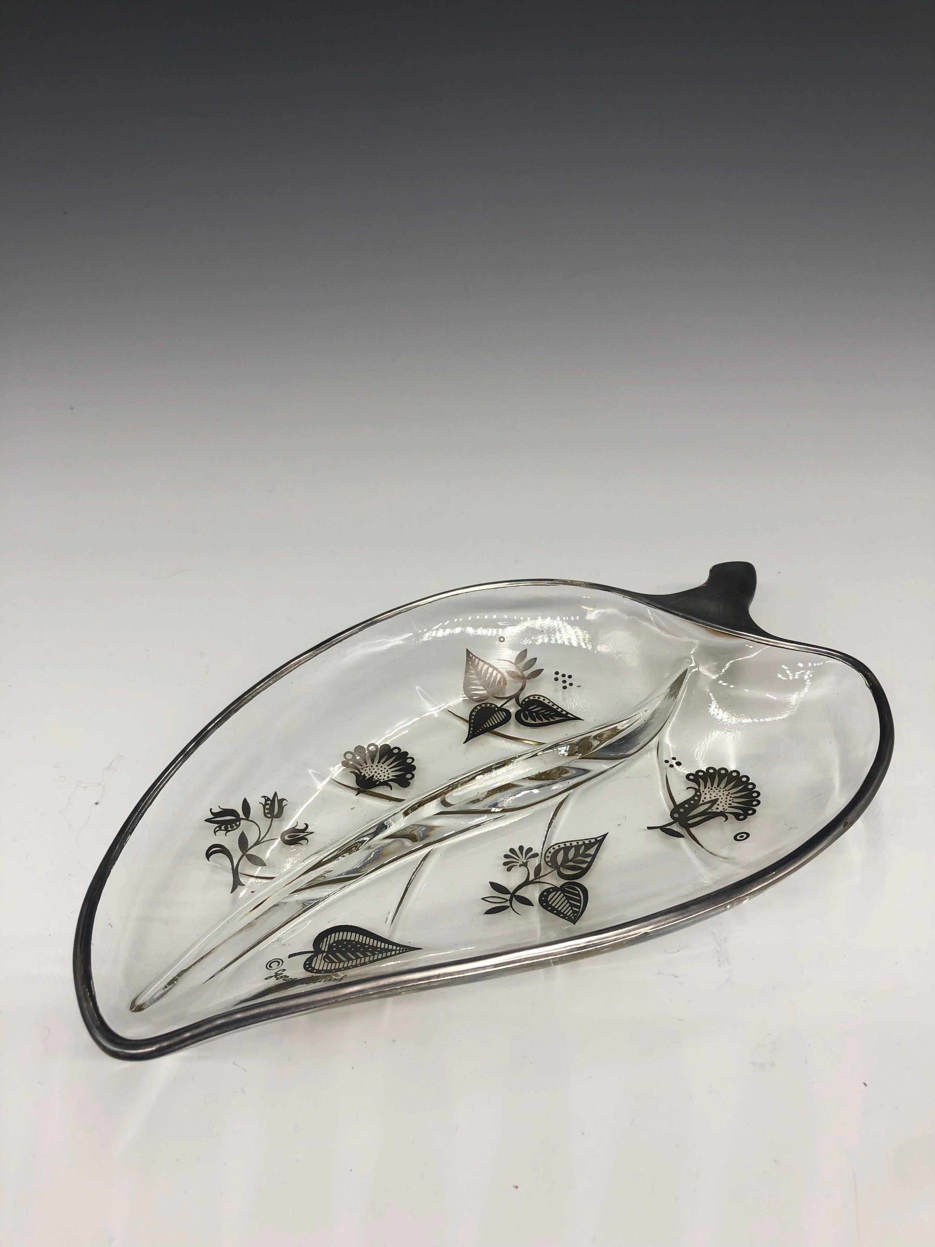 Vintage 1960s Georges Briard clear leaf shape tray/dish with silver floral detail. The piece has a divider that goes down the center. Signed lower right. It can be used as a candy, nut, relish dish, or a catch-all. 

Georges Briard was an American