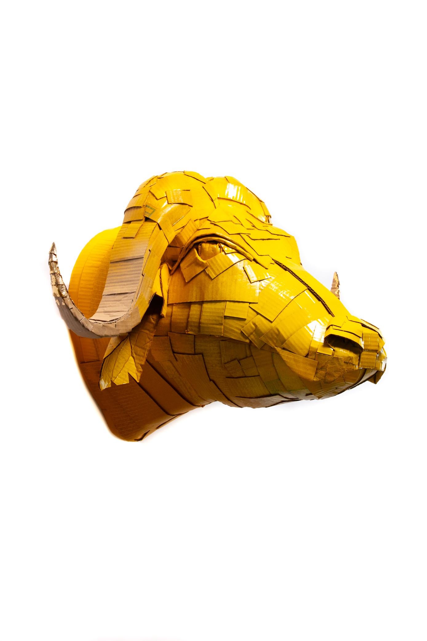 Grande sculpture de tête de buffle jaune caramel avec des détails de corne en feuille d'or, méticuleusement créée par l'artiste Justin King à partir de morceaux de carton et de papier mâché découpés et pliés individuellement. Le choix des couleurs