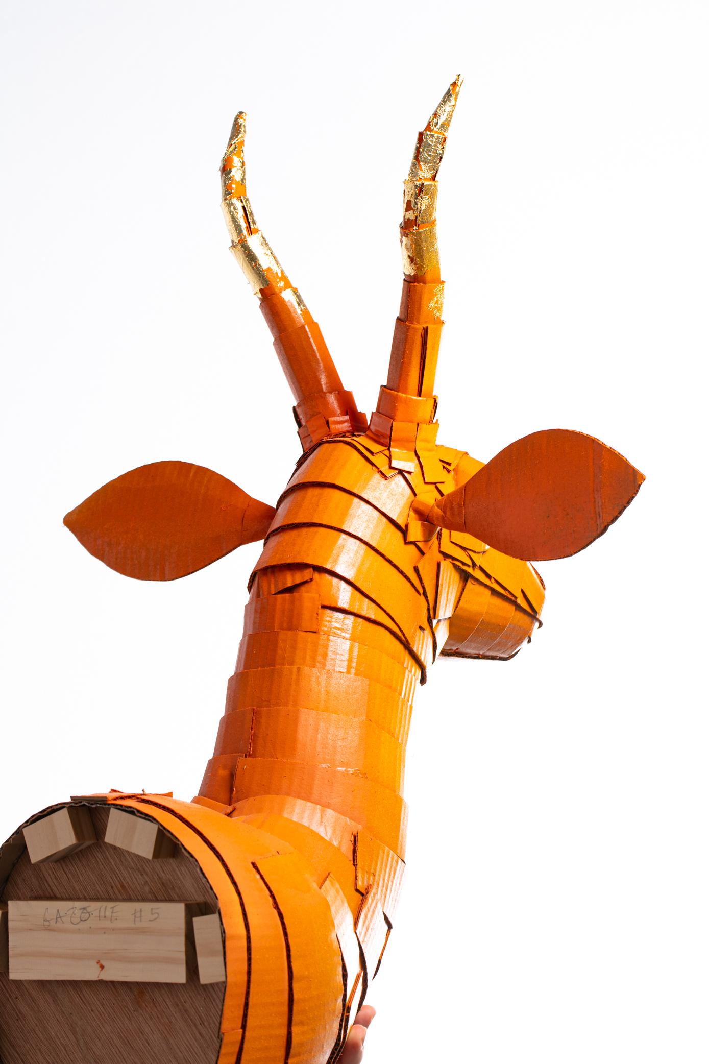 Gazelle sculpture in Persimmon Orange with Gold Leaf Horn Detail meticulously created by Artist Justin King from individually cut and folded pieces of cardboard and papier-mâché. King’s choice of color and ornamental detail emphasize the spirit of