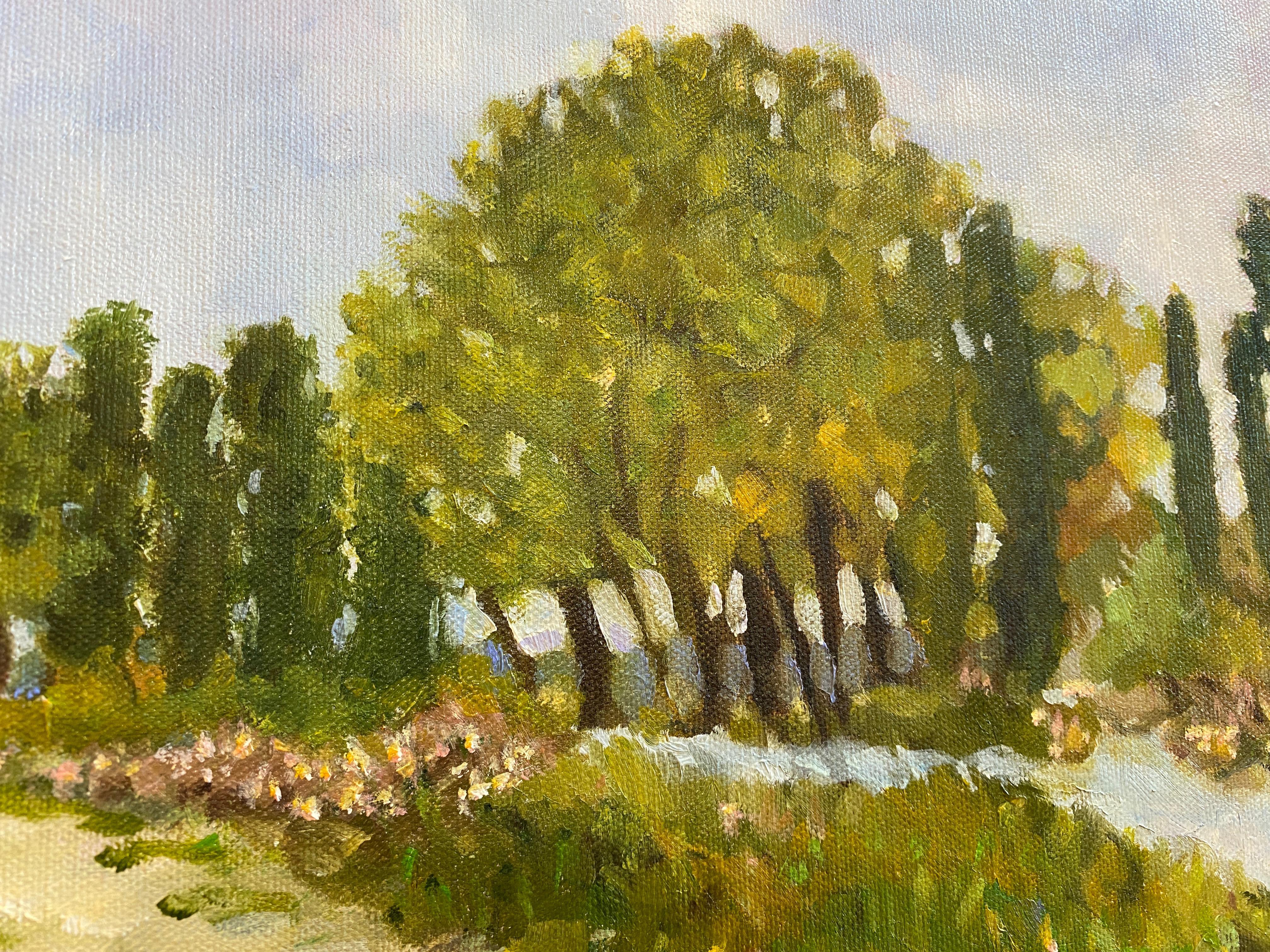 This landscape painting depicts a calm, serene water view with a predominant cumulus cloud-filled blue sky of summer. A green tree-lined beach lane with pink flowers is the central focus of the painting inviting the viewer to enter the sandy trail