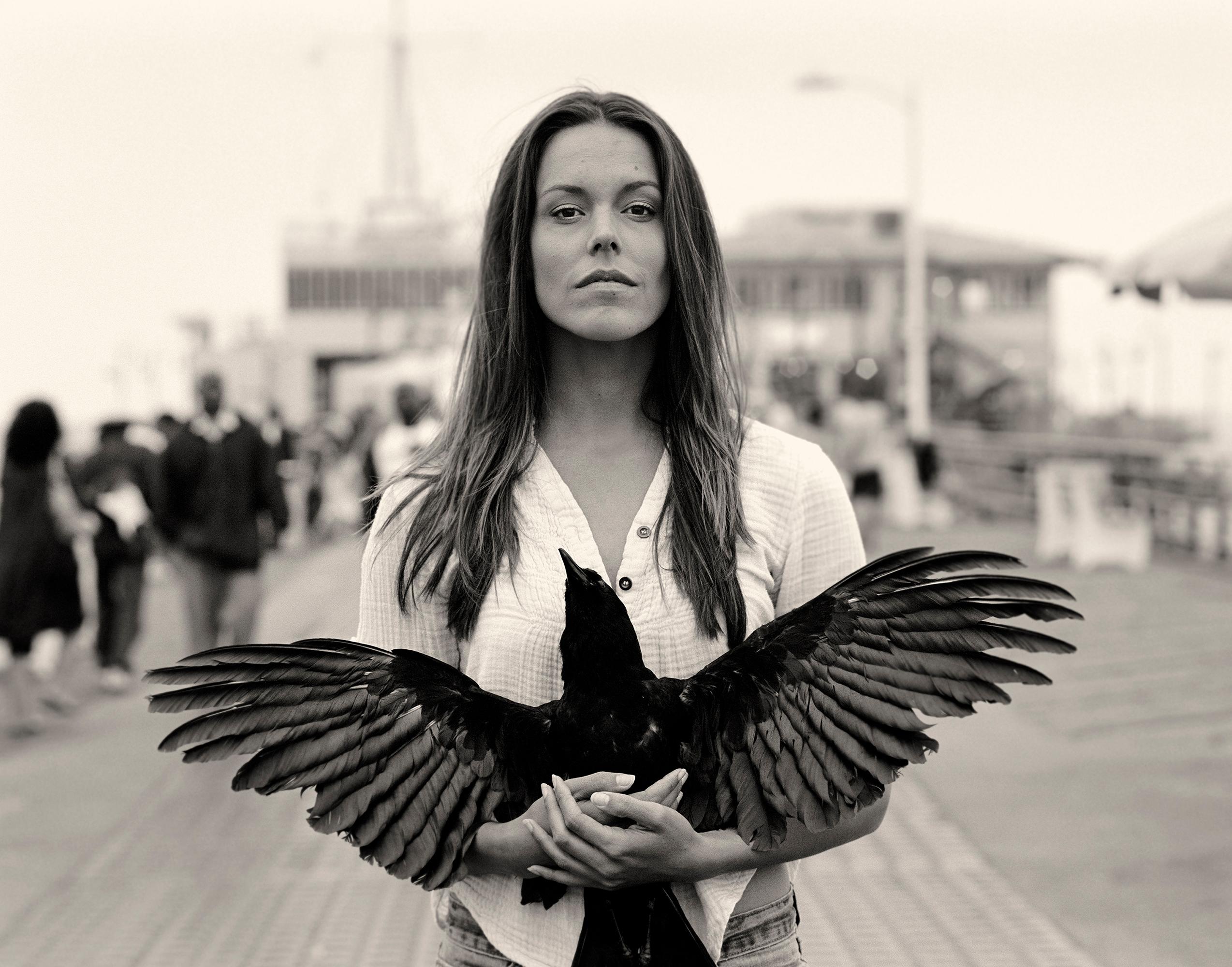 'Tawney' is from the series of archival black and white photographs by the artist, 'Between Two Worlds.' In this photograph, a central female figure confronts the viewer directly holding a large black spread-winged bird. This giclee is  #1 in an