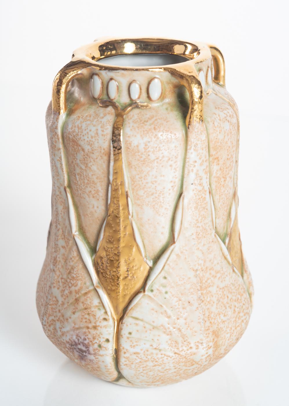 Delicate textured vase featuring geometric gingko leaves in a repeating pattern, with gold gilt arms and mouth. Ernst Wahliss vase with a design attributed to Paul Dachsel. 

Already well established throughout Europe as a retailer of porcelain