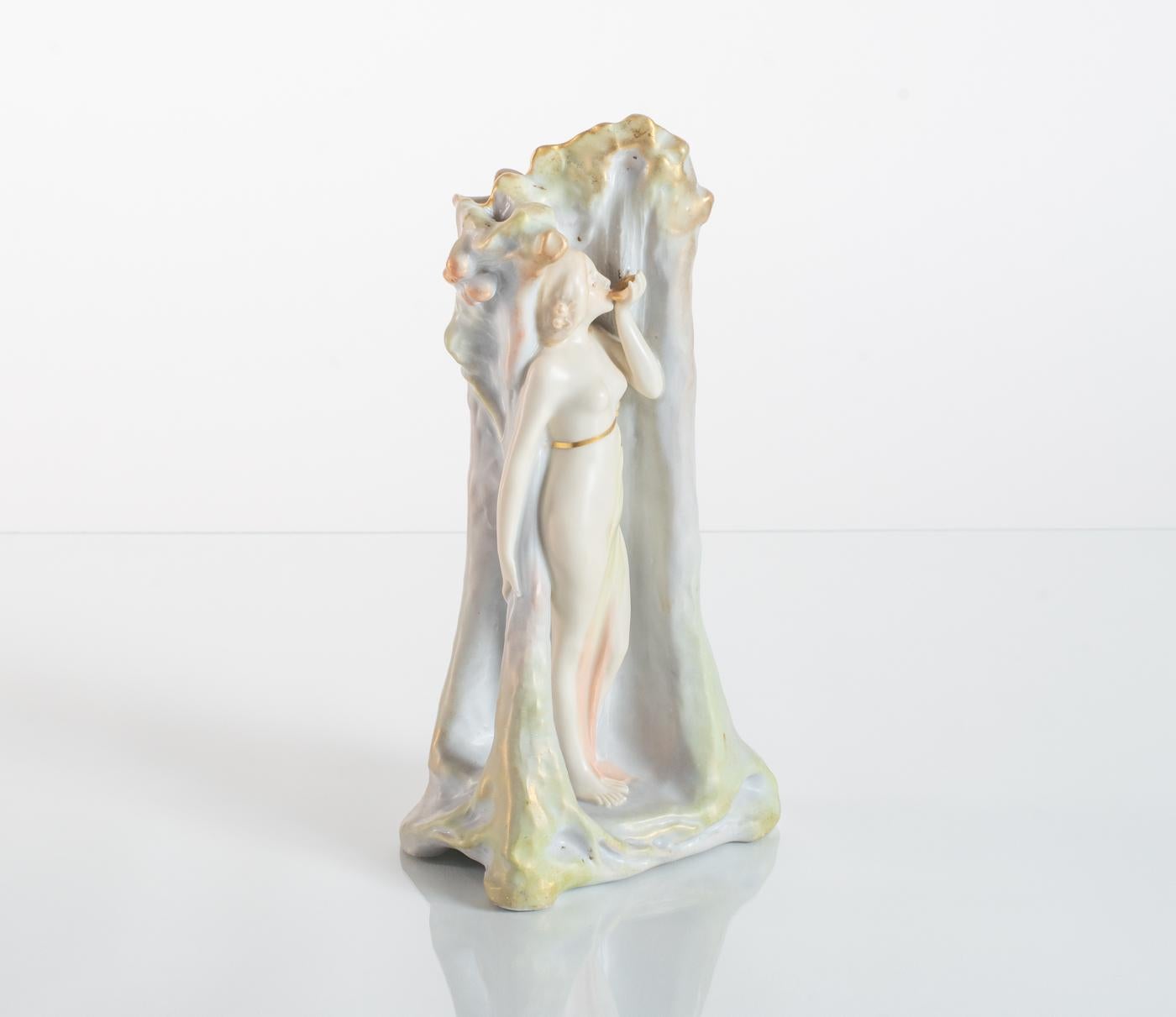 Austrian Art Nouveau vase featuring a maiden standing at the base of a tree, drinking from a leaf, with gentle shades of green and blue. An excellent example of the "ivory porcelain" ceramic material being used by producers in the Turn-Teplitz area.