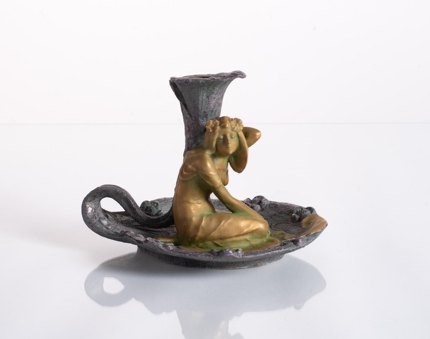 Figural candlestick with a golden maiden on an iridescent form. This ceramic features a beautiful juxtaposition of the smooth texture of the woman against a psychedelic stone-like flowerbed, with an open tulip ready to receive a candle. Stamped