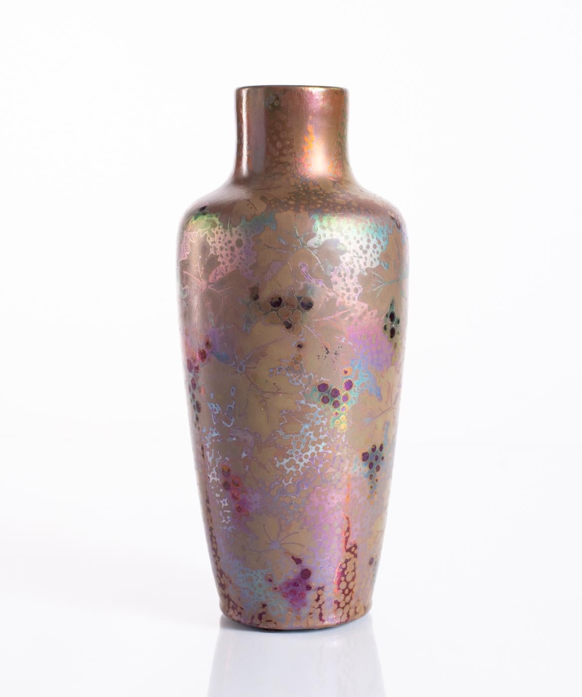 Vase en céramique à glaçure métallique bleue et verte du maître de l'irisation Clément Massier, avec des grappes de raisin et des feuilles d'un violet profond. Signé MCM dans la base, et numéroté. 

Clément Massier était un célèbre céramiste