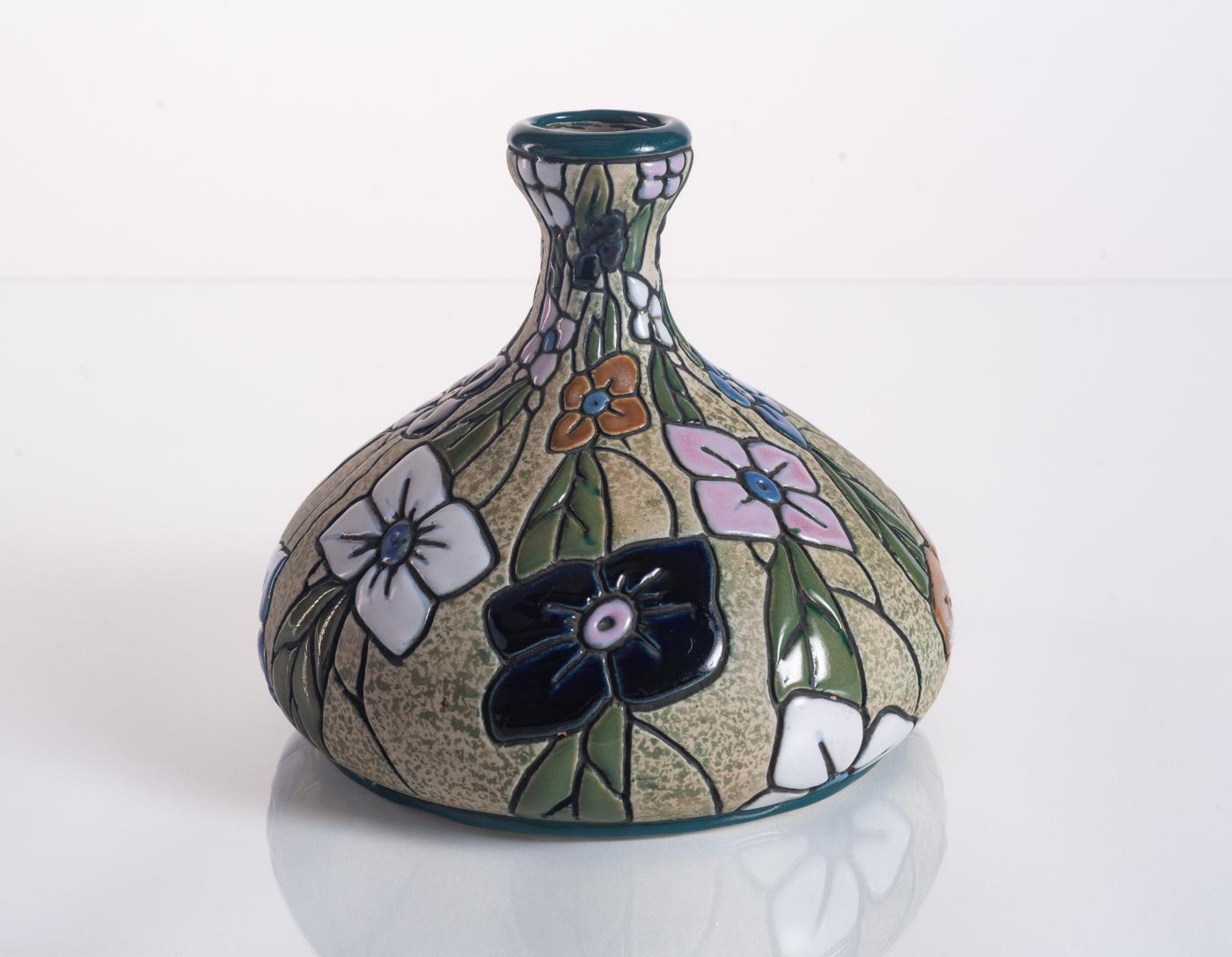 Eine farbenfrohe Keramikvase mit handgemalten Blumen in leuchtender Cloisonné-Emaillierung. Amphora im Sockel gestempelt und nummeriert.

Riessner, Stellmacher und Kessel (RStK), später bekannt als Amphora, begann 1892 in Turn-Teplitz, Österreich,