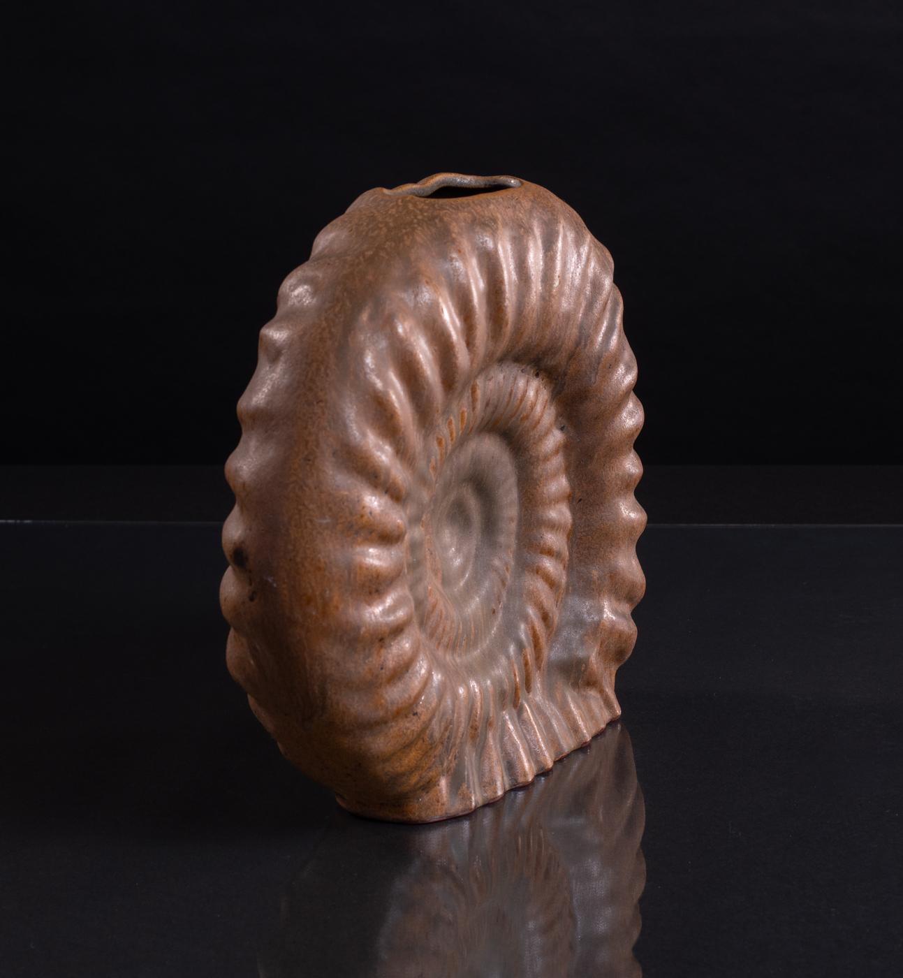 Handglasierte, ammonitenförmige Vase von Helmut Schäffenacker in einer tiefen Rostfarbe. Im Sockel nummeriert. Formular V-6. 

Helmut Schäffenacker gründete das Atelier Schäffenacker im Jahr 1948 in Westdeutschland. In seinem Studio arbeitete er mit
