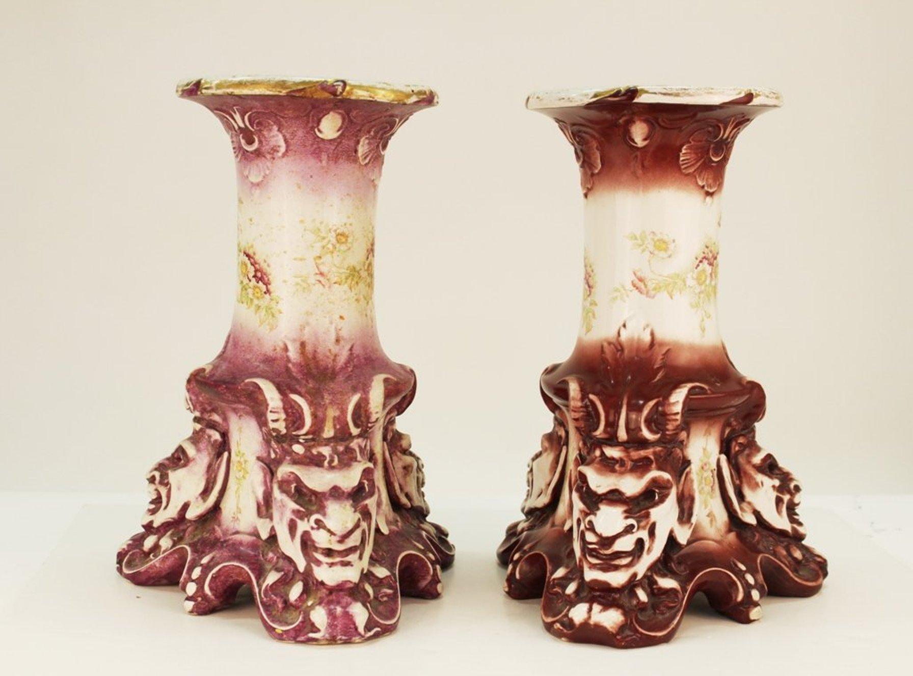 Victorian period hand-painted ceramic pedestals in grotesque style with horned satyr heads at the base, made by Alba China. The pair is stamped at the bottom with a mark reading 'Bona fama est mellor zona aurea' ('A good reputation is better than a