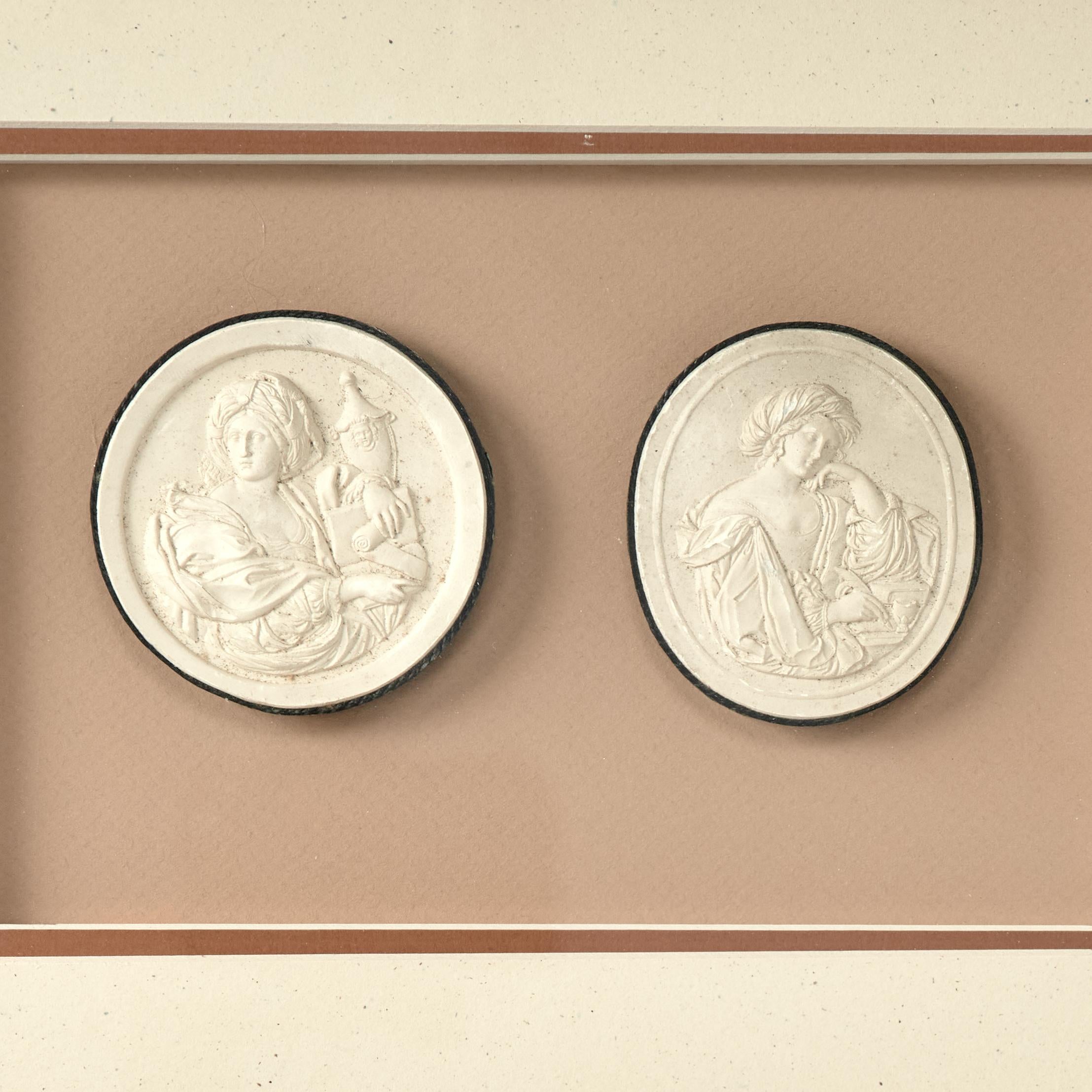 Ecco due cimeli neoclassici dell'educazione aristocratica nota come Grand Tour, una coppia di intagli in gesso, accoppiati e presentati sotto vetro in una cornice di legno dorato. 