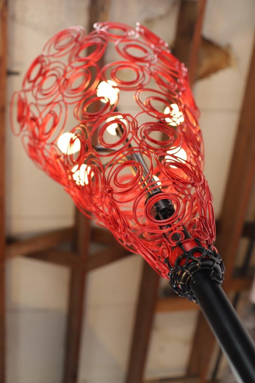 This beautiful modern lamp by contemporary artist Susan Woods is both a unique piece of art and a functioning design element. 

The lamp is made out of conical upholstery springs, steel, cast iron and is powder coated red and black. Its three main