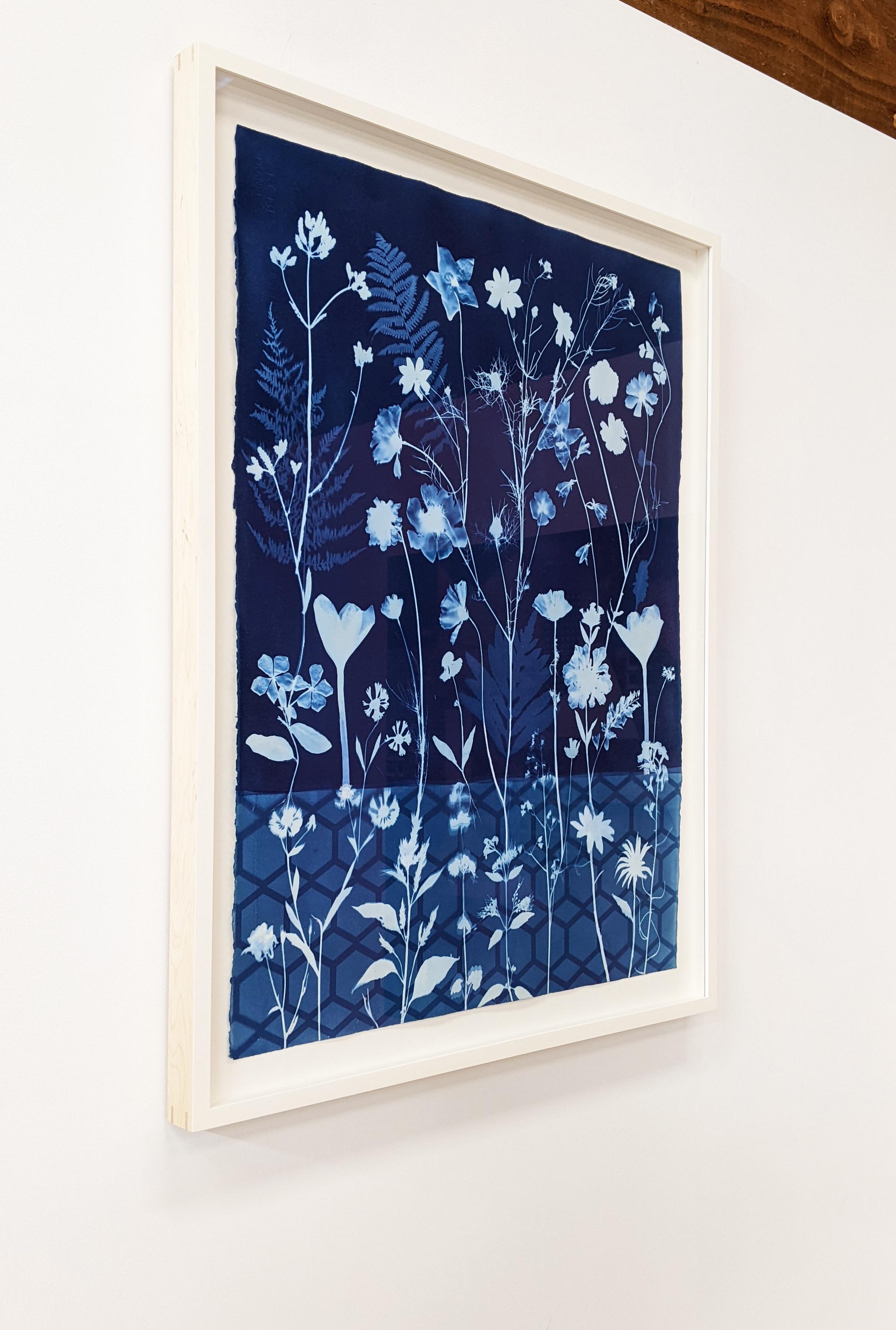 In this vertical work in watercolor, ink, gouache, and cyanotype on Arches platine paper, meticulously detailed flowers, including crocus, star flower, cosmos and ferns are depicted in shades of pale blue against a deep, indigo blue background with