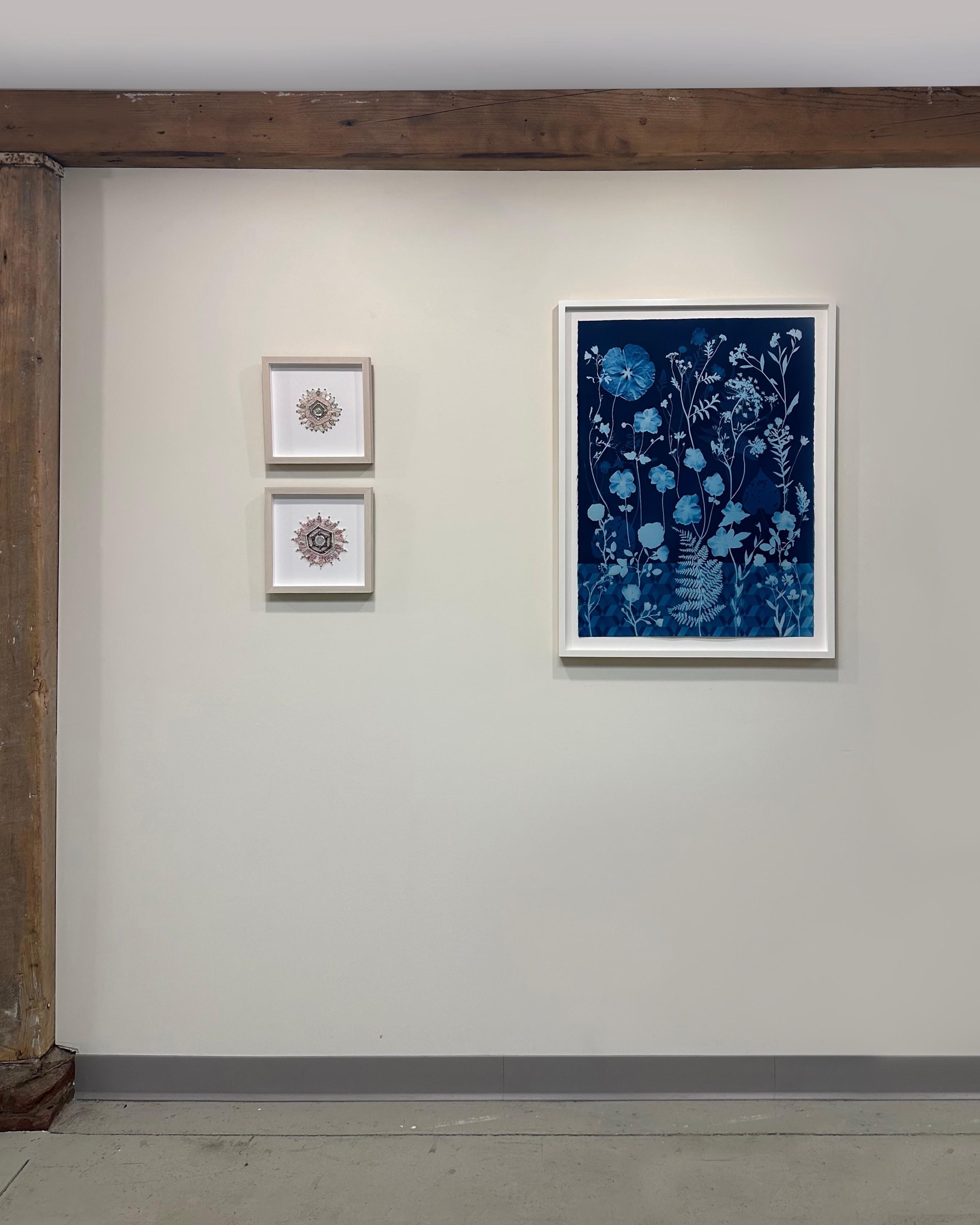 In watercolor, ink, gouache, and cyanotype on Arches platine paper, meticulously detailed flowers, including anemones, rose of sharon, and queen anne's lace are depicted in shades of pale blue against a deep, indigo blue background with a geometric