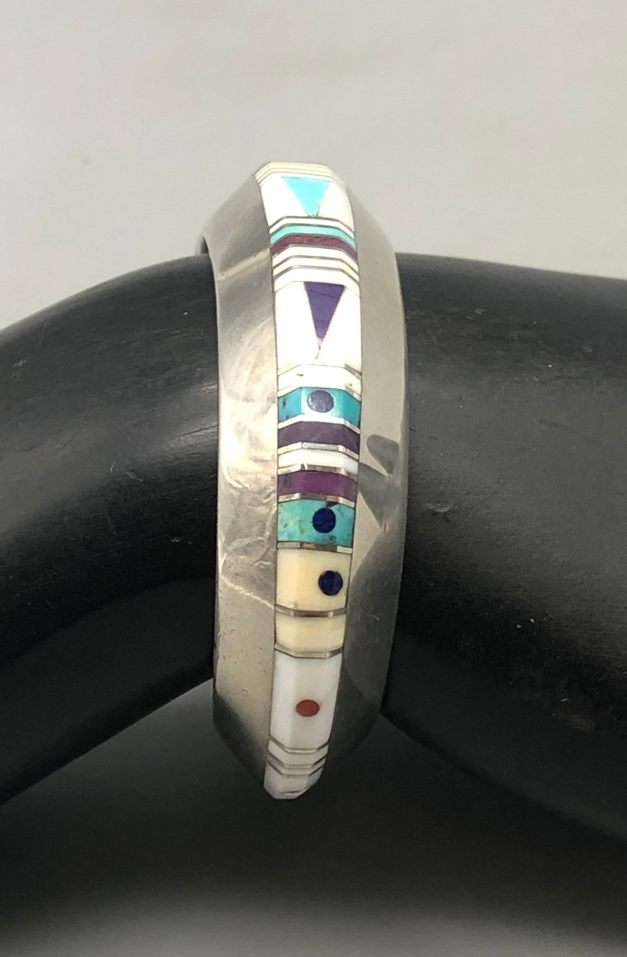 Gibson Nez Multi Stone Inlay Bracelet

This geometric shaped bracelet, by award winning artist Gibson Nez, features a channel inlay design created with turquoise, lapis, coral, onyx and so many other stones. The stones are separated by fine silver