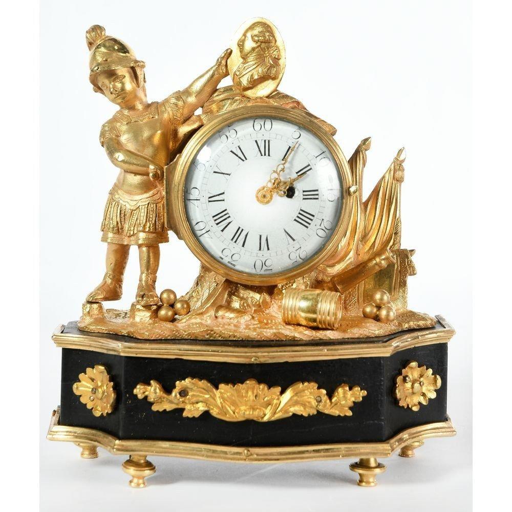 "LOUIS XVI CLOCK François Duchêne Received Master In 1733"

LOUIS XVI CLOCK in gilded bronze representing a helmeted man holding a profile of King Louis XVI above the enamelled movement. On the right, a cannon, balls and various flags. Blackened