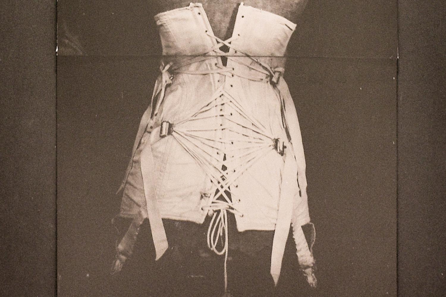 Vintage still life photograph of a white antique corset on black 

