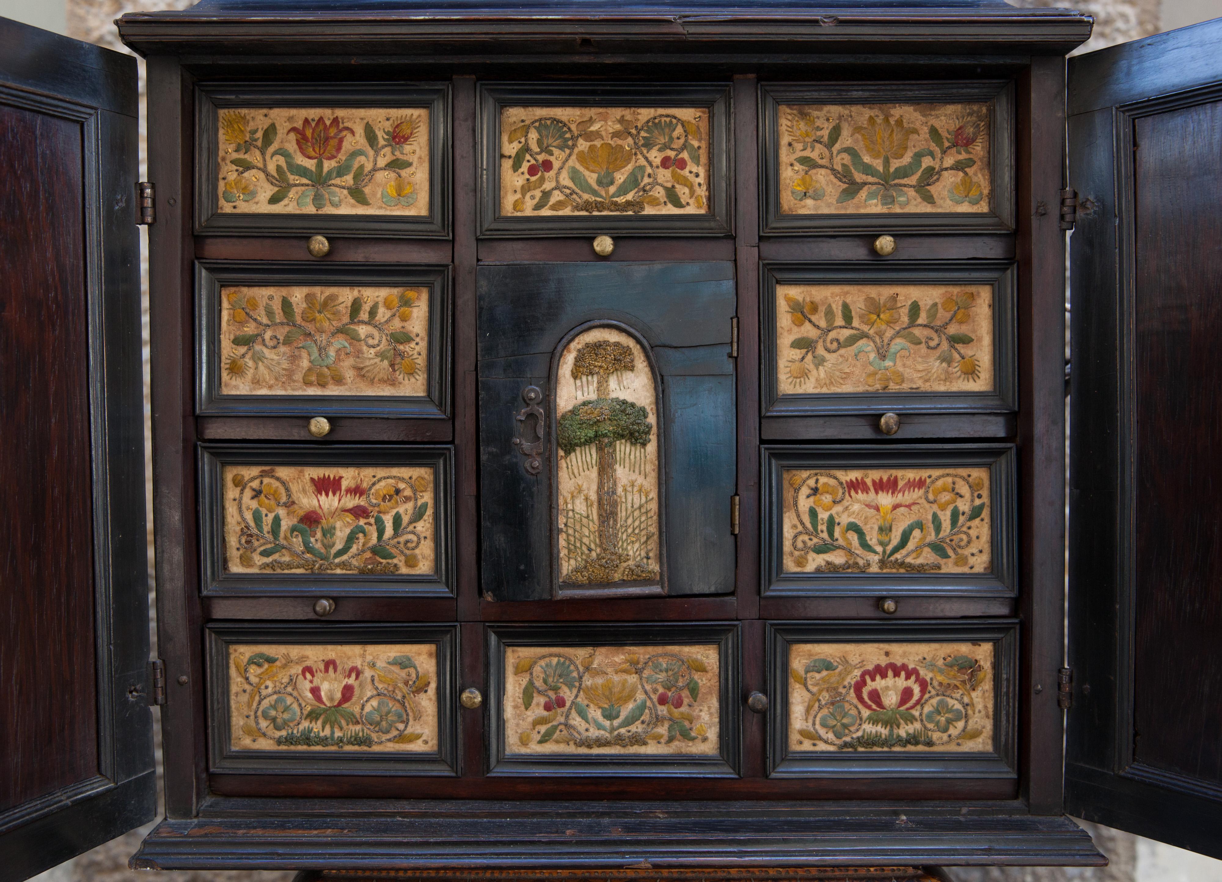 Collector's Cabinet.
Antwerp.
XVIIth century.
Ebony, wood (oak?) embroidered silk.
Restored, with some imperfections.

Two doors and top lid with locks.
Small upper drawers and one large lower drawer.

The choice of ebony and silk reflect the taste