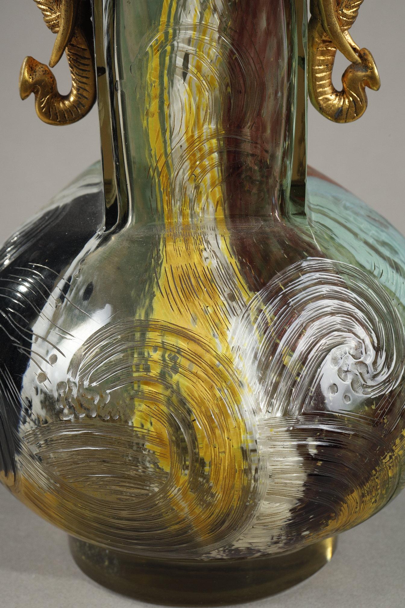 Vase with Elephant heads
attributed to
Eugène ROUSSEAU (1827-1890) 
and Ernest LEVEILLE (1841–1913)

A blown glass vase,
decorated in relief with stylized swirls
Decorated with polychrome stains in the glass
Flanked by gilded bronze Elephant