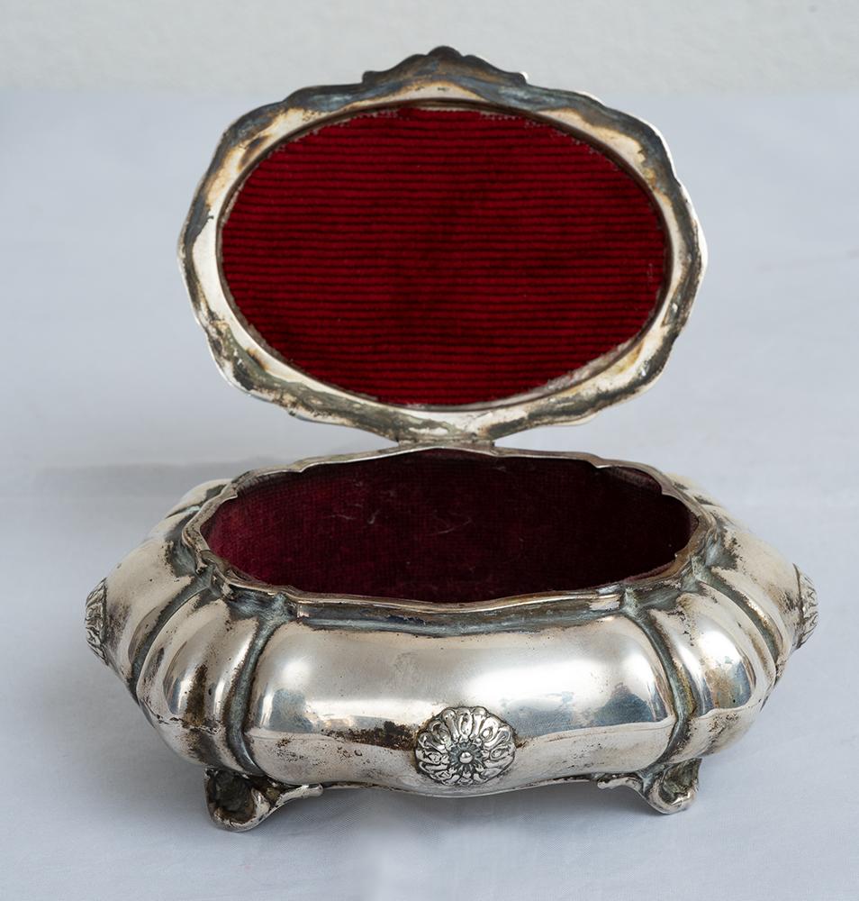 Neapolitan silver jewelry box belonging to the early 20th century.

The lid features a central ruby-colored hard stone while the central body has multiple domes alternating with chiseled reliefs.

The four feet have a shell shape.

Weight: