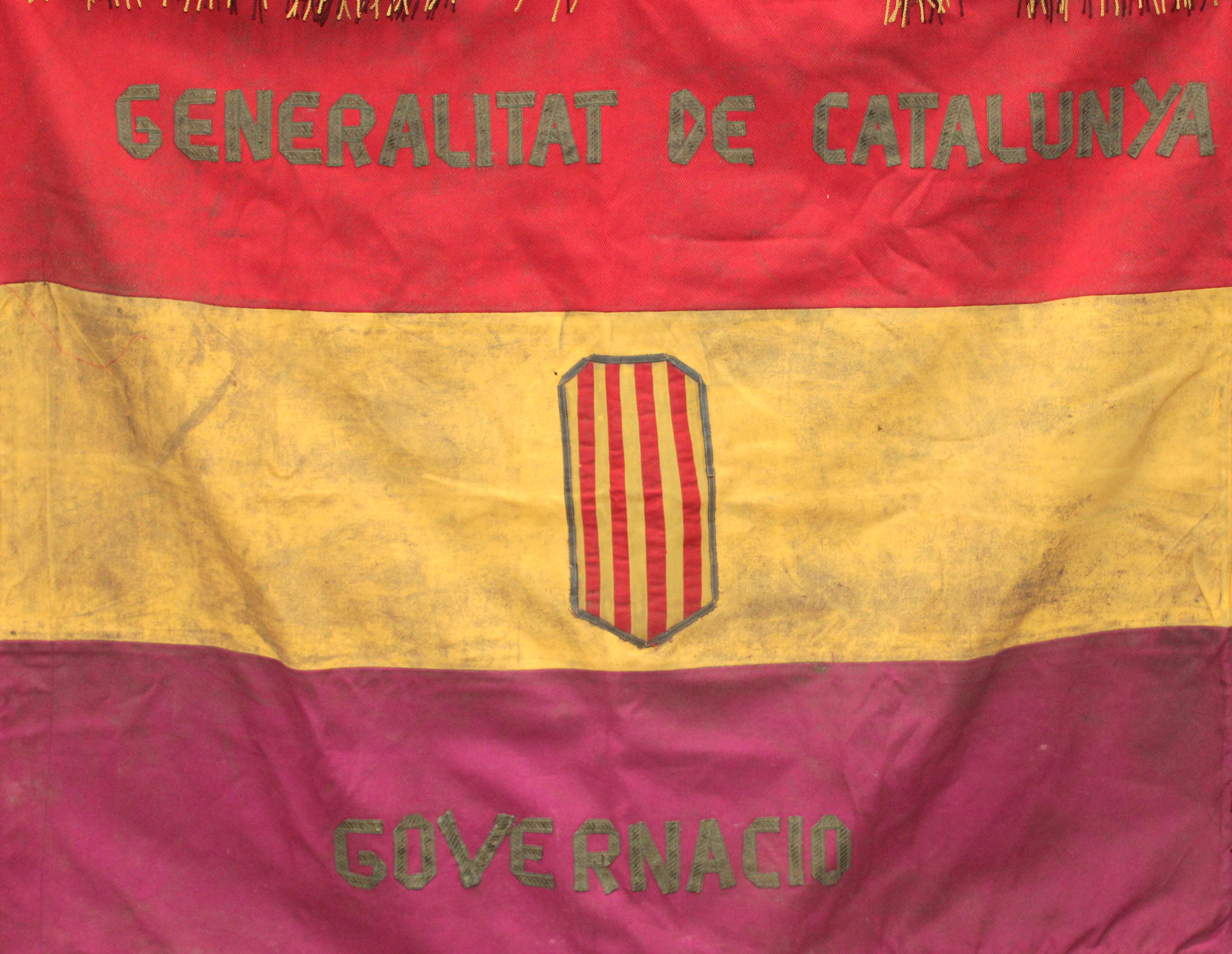 La bandera exhibida está compuesta por tres franjas horizontales de igual tamaño. La franja superior es de color rojo intenso, la central de color amarillo dorado y la inferior de color grana oscuro. Todas las franjas tienen flecos dorados en la