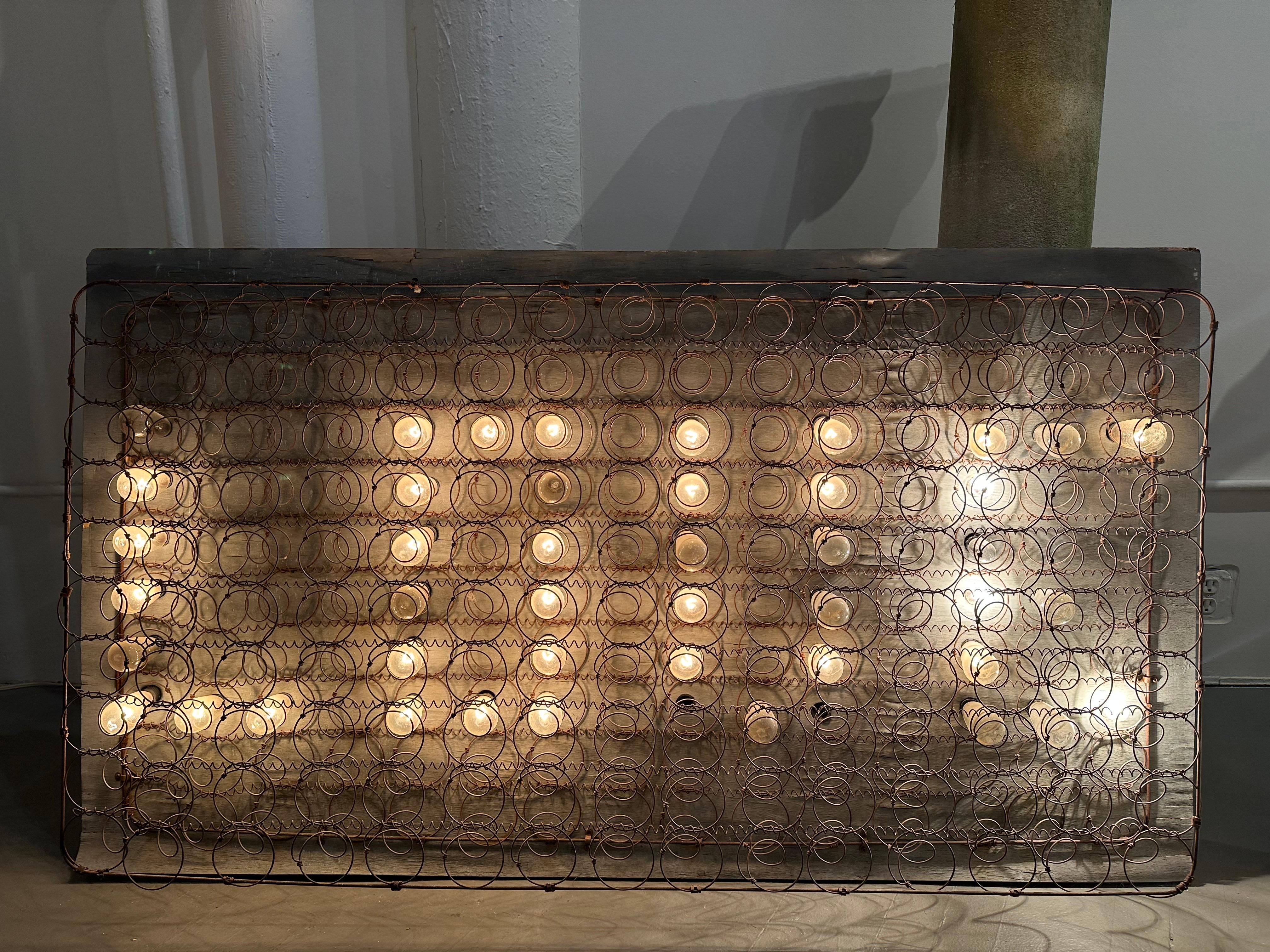 Cette remarquable installation lumineuse murale est fabriquée à partir d'un cadre de sommier vintage récupéré et équipée d'ampoules chaudes, formant le mot 