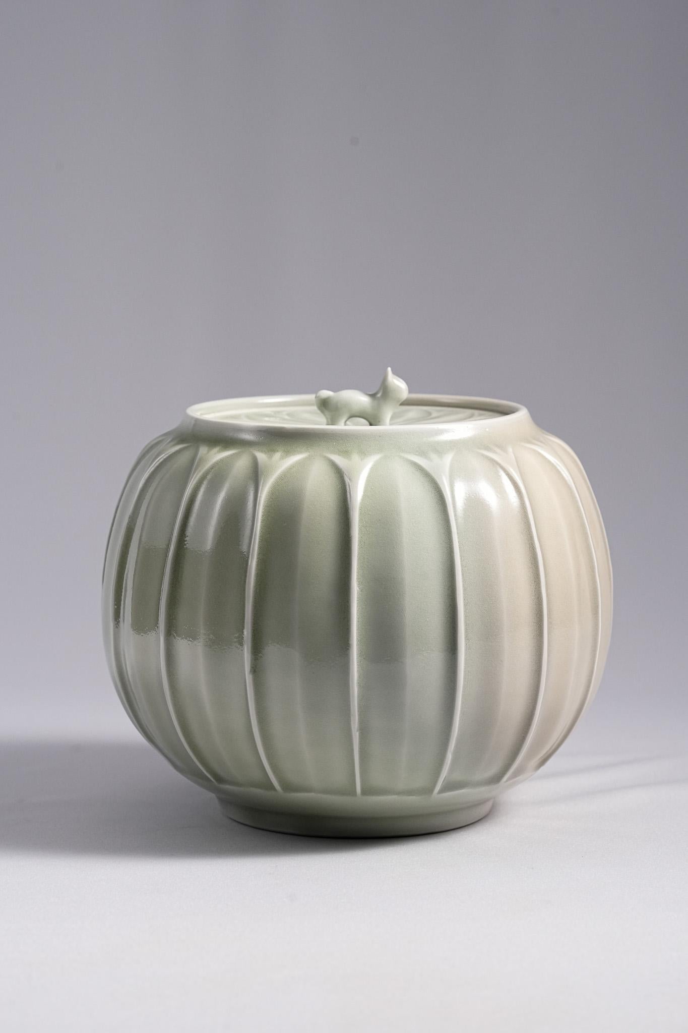 This Celadon Water Jar was created by Living National Treasure Kiyoshi Hara. The form is rounded and elegant, covered entirely in a soft pale-green celadon glaze that radiates a gentle, jade-like luster. The surface features melon-ribbed lines that
