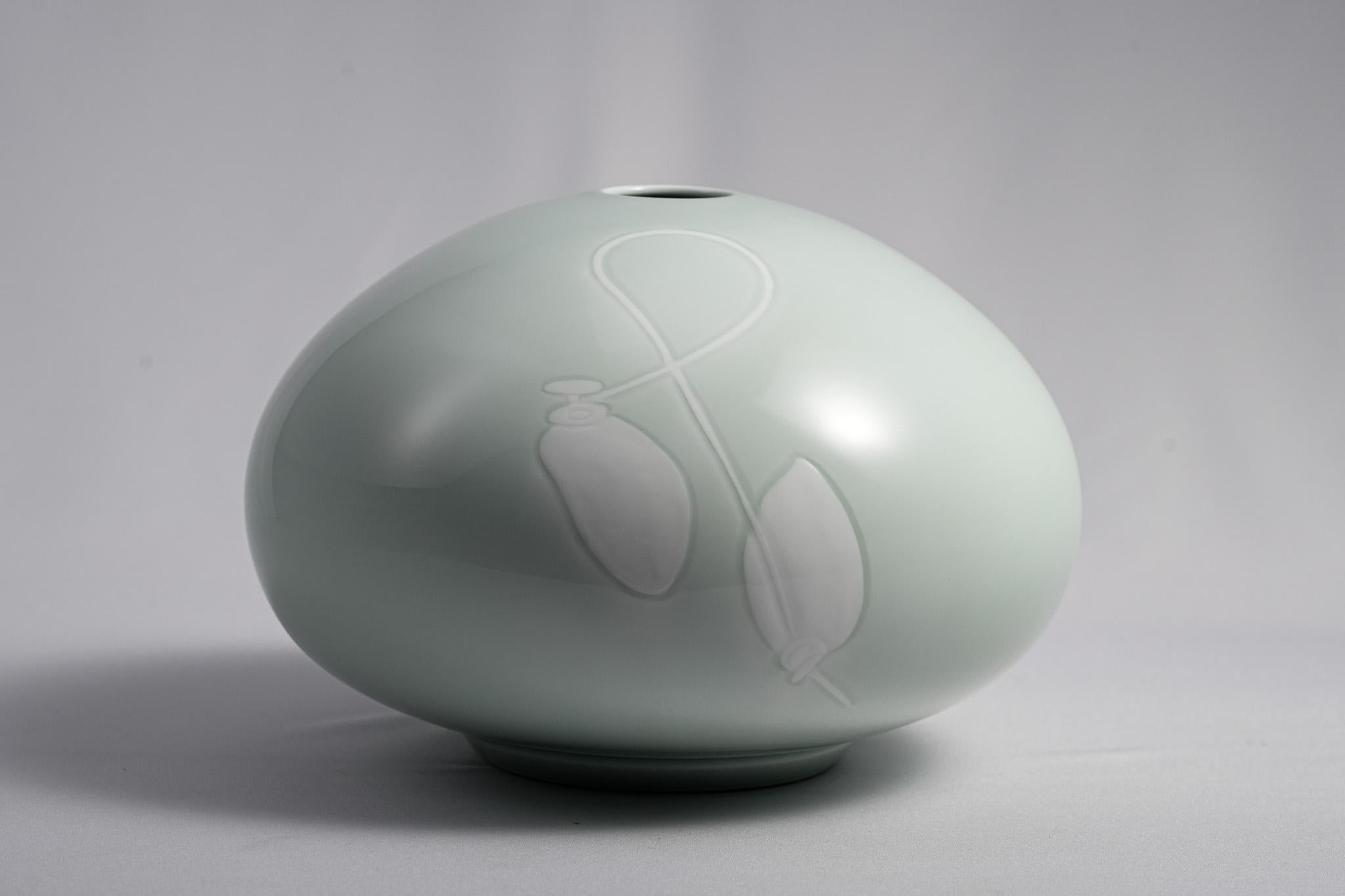 Die Celadon Persimmon Vase von Living National Treasure Manji Inoue verkörpert stille Anmut und raffinierte Schönheit. Die runde Form ist mit einer weichen, durchscheinenden Seladonglasur überzogen, die in einem sanften, jadeähnlichen Licht