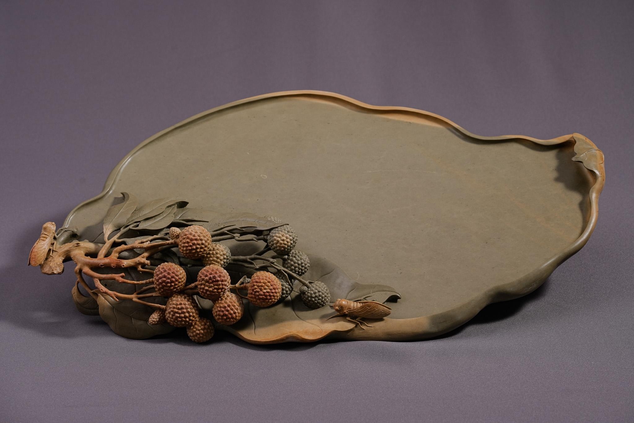 Lychee Abundance, The Auspicious Fortune Desk Ornament wurde 2012 von Meister Gui Yang Mo aus feinem grünen Duan Stein geschnitzt. Der Duan-Stein ist einer der vier berühmten Tuschesteine Chinas, der für seine glatte Textur und seine hervorragenden