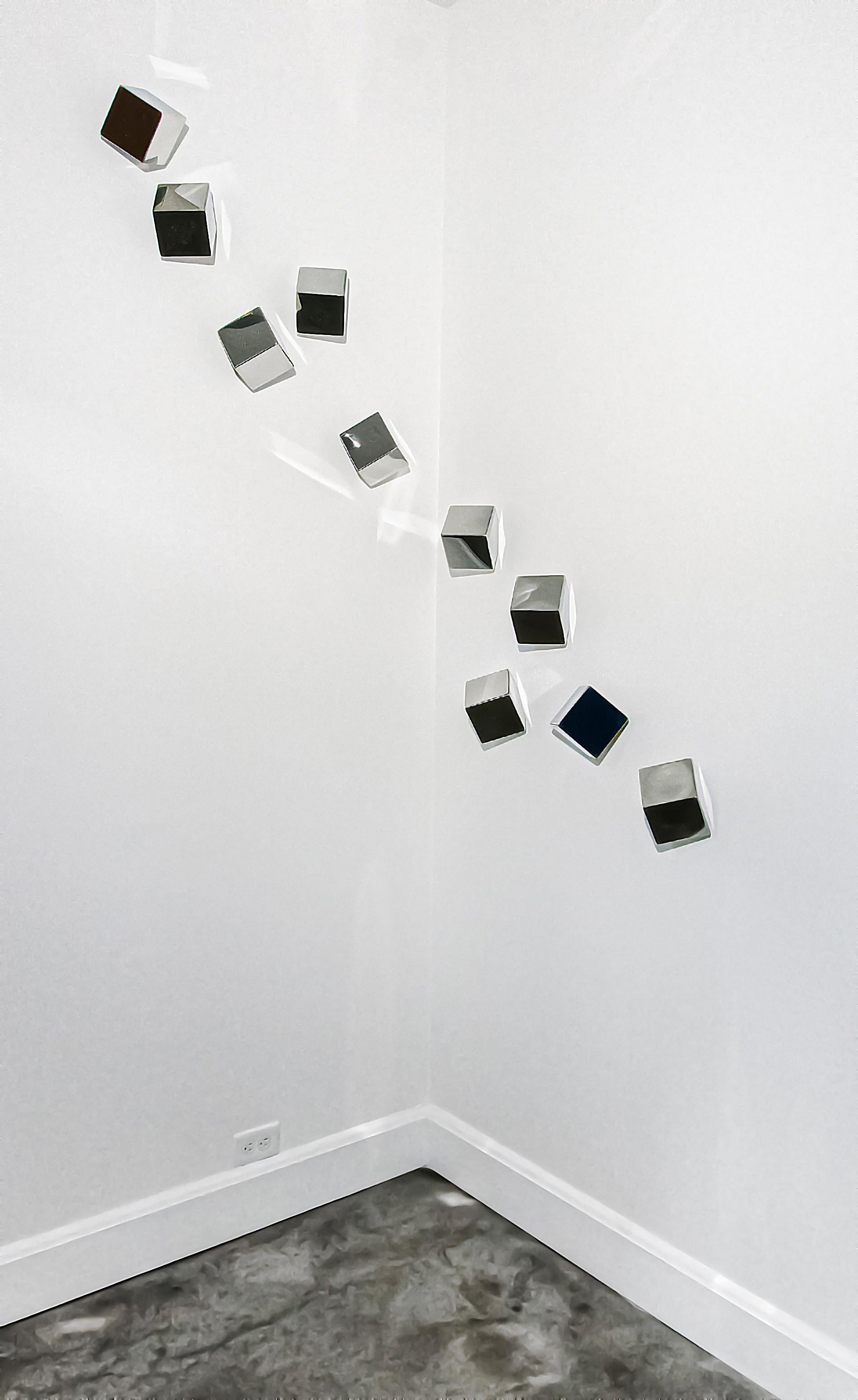 Ten reflective stainless steel cubes drift across the wall in this dazzling sculpture by California artist, Lori Cozen-Geller. Her minimalist work is inspired by everyday life and its emotions. Change is part of a series created by the artist after