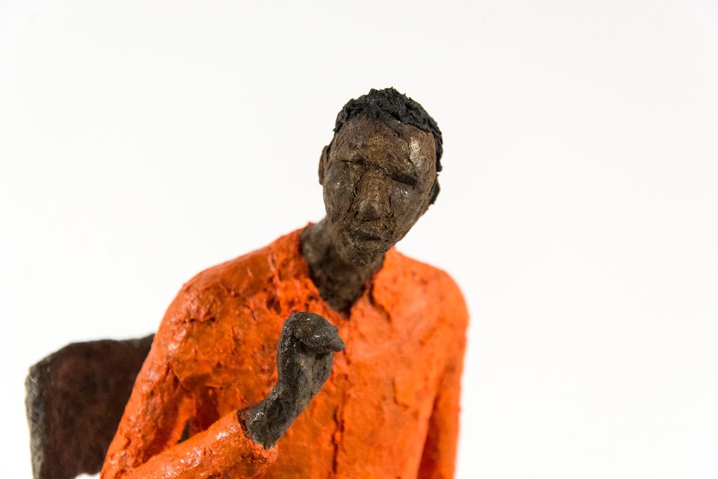A pair of seated figures in a blue and orange wait patiently in this contemplative paper mache sculpture by Paul Duval. 

Paul Duval is a member of the Canadian Sculptors Society and of the Conseil de la sculpture du Québec. He studied Monumental
