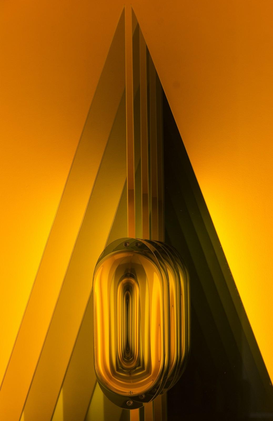 Utilizing mirrored reflections and glowing amber light, Acute Triangle features an infinitely receding ovular ring nested in and infinitely receding isosceles triangle. Like a glowing porthole into an alternate reality, Emig's work mesmerizes the