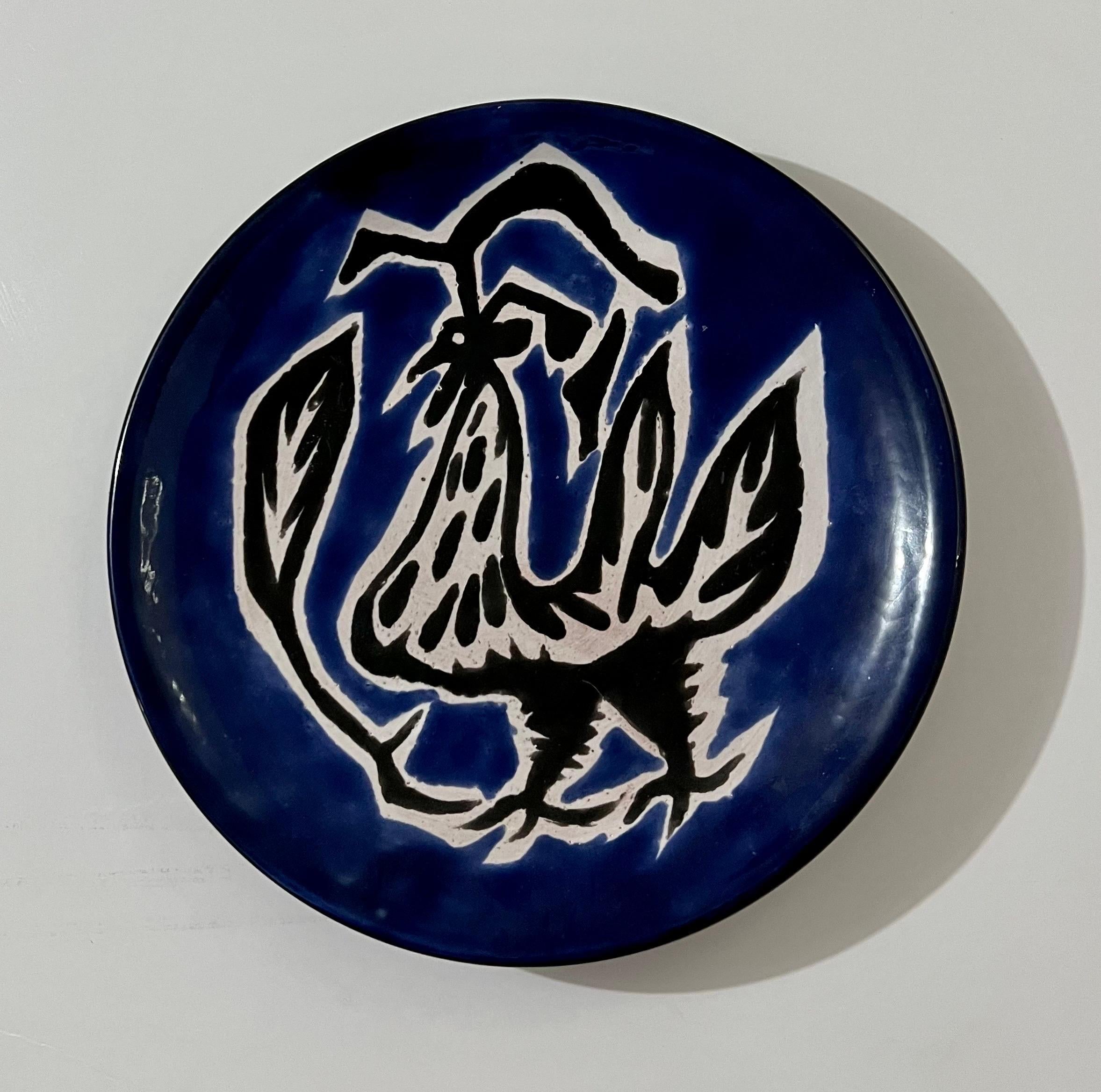 Vintage Jean Lurcat glazed fired enamel wall plaque ceramic plate limited edition hand inscribed faience Ceramique Saint Vicens charger.  It depicts a highly stylized rooster, le coq, in bright, vibrant cobalt blue colors.
Jean Lurçat (French: 1892