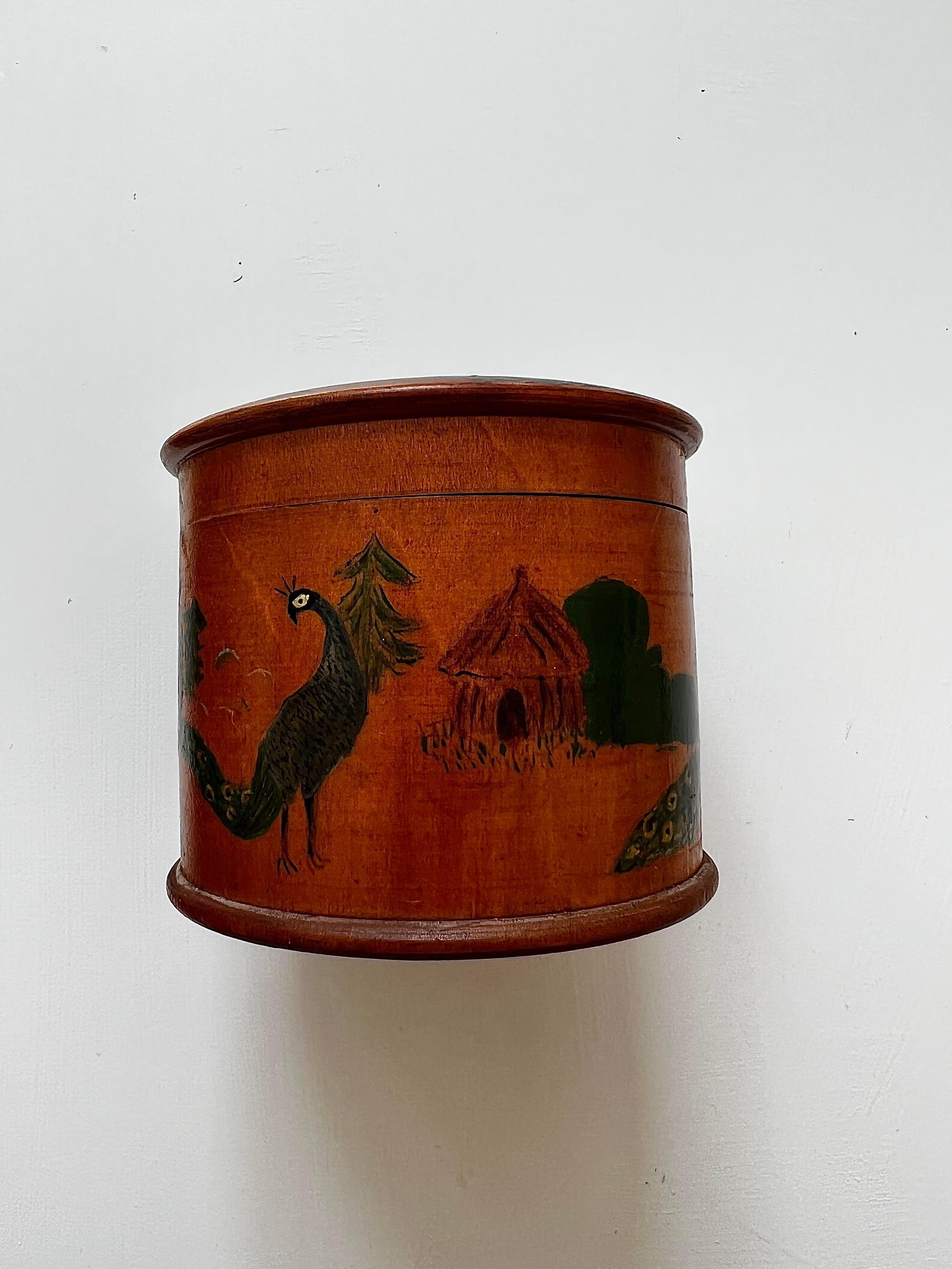 This Victorian wooden string box is very intricately painted by hand. There are beautiful scenes featuring peacocks around the box and a peacock with outstretched feathers on the lid. At the bottom of the box is a stamp reading 