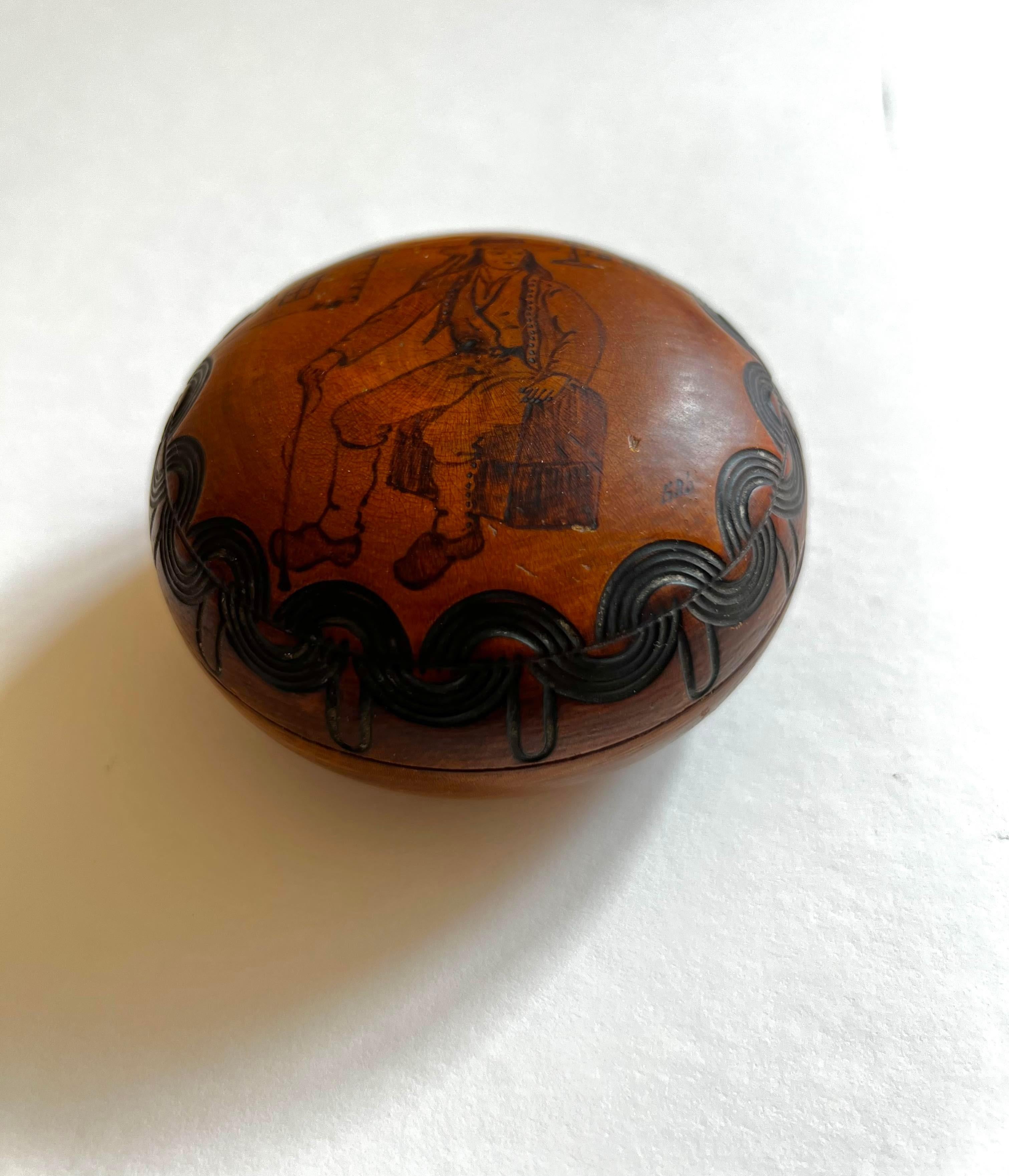 This honey colored wooden box depicts a breton figure in traditional clothing. Brittany is the northwesternmost region of France, heavily influenced by Celtic culture and was a part of the Roman Empire. This ovular spherical box is meticulously